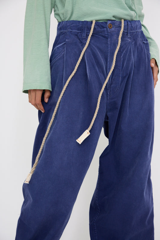 A person is dressed in a light green long-sleeve shirt and oversized Dr. Collectors P40 Z Boy's Twill Pant in Sunfaded Sailor Blue crafted from Japanese cotton, cinched comfortably with a rope belt against a white background.