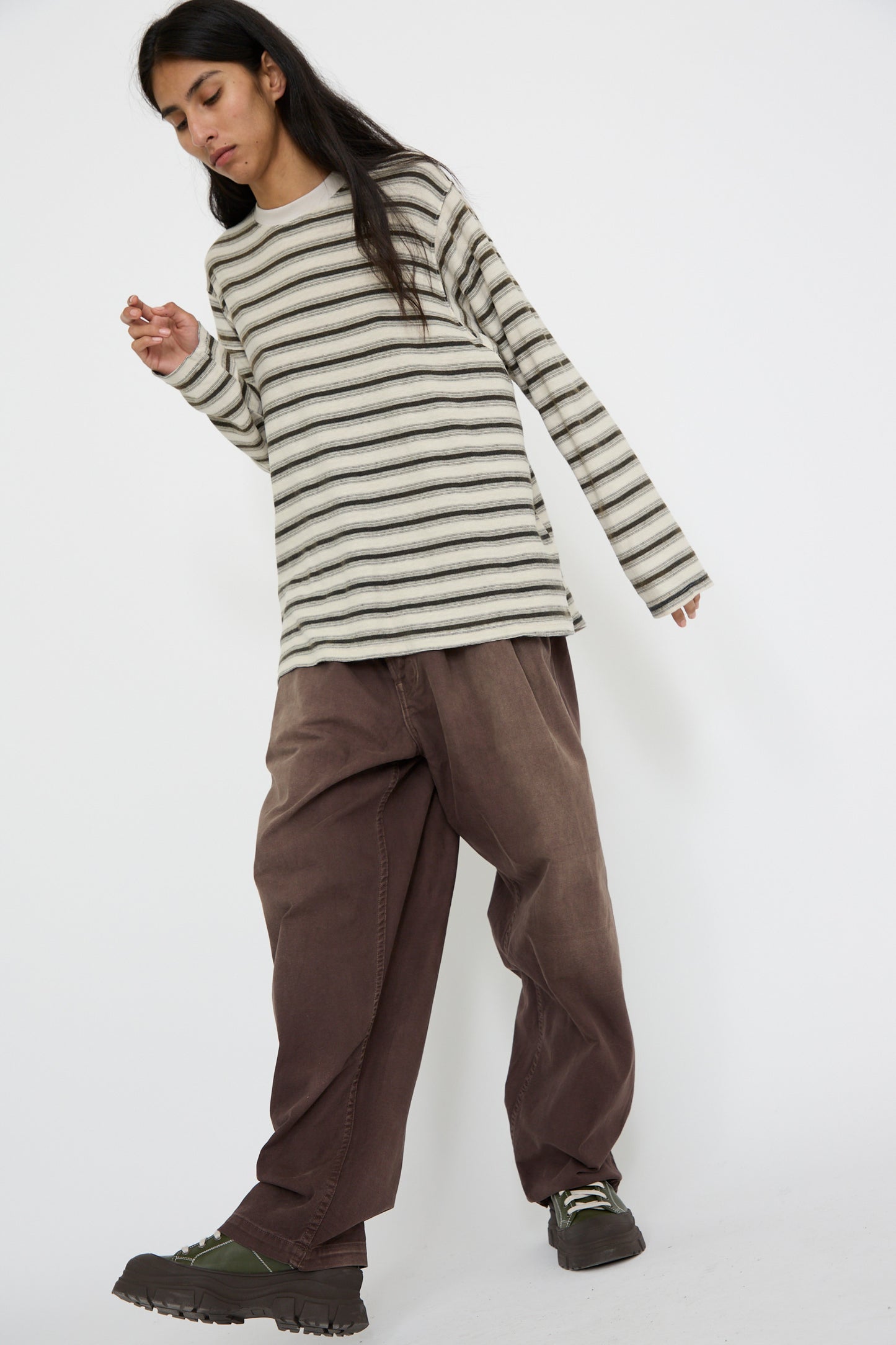 A person wearing a striped long-sleeve shirt, Dr. Collectors' P40 Z Boy's Twill Pants Sunfaded in Cappuccino with an elasticated waistband, and rugged brown shoes strikes a casual pose against a plain background.