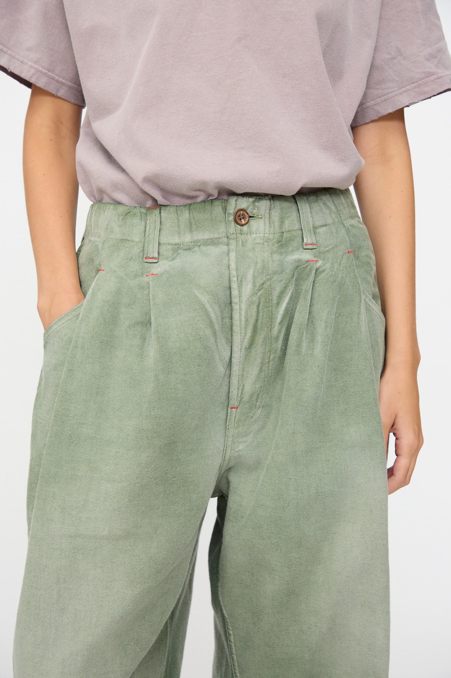 A person wearing a loose-fitting, light purple short-sleeve shirt and Dr. Collectors P40 Z Boys Pant in Sunfaded Army Green—crafted from soft Japanese cotton with a relaxed, high-waisted fit—hands in pockets, photographed from shoulders to knees.