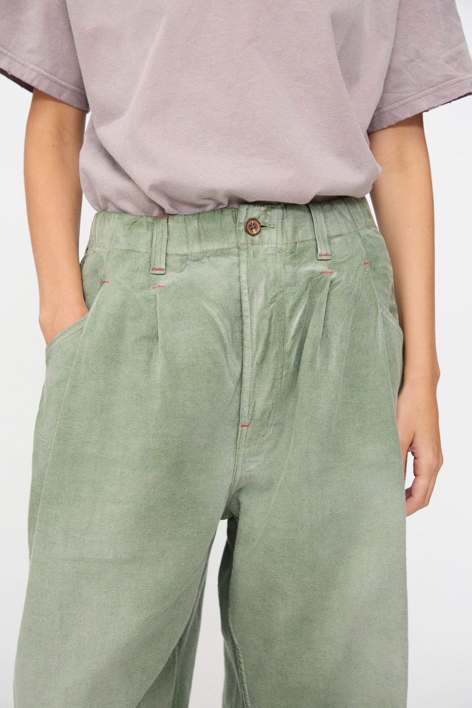 A person wearing a loose-fitting, light purple short-sleeve shirt and Dr. Collectors P40 Z Boys Pant in Sunfaded Army Green—crafted from soft Japanese cotton with a relaxed, high-waisted fit—hands in pockets, photographed from shoulders to knees.