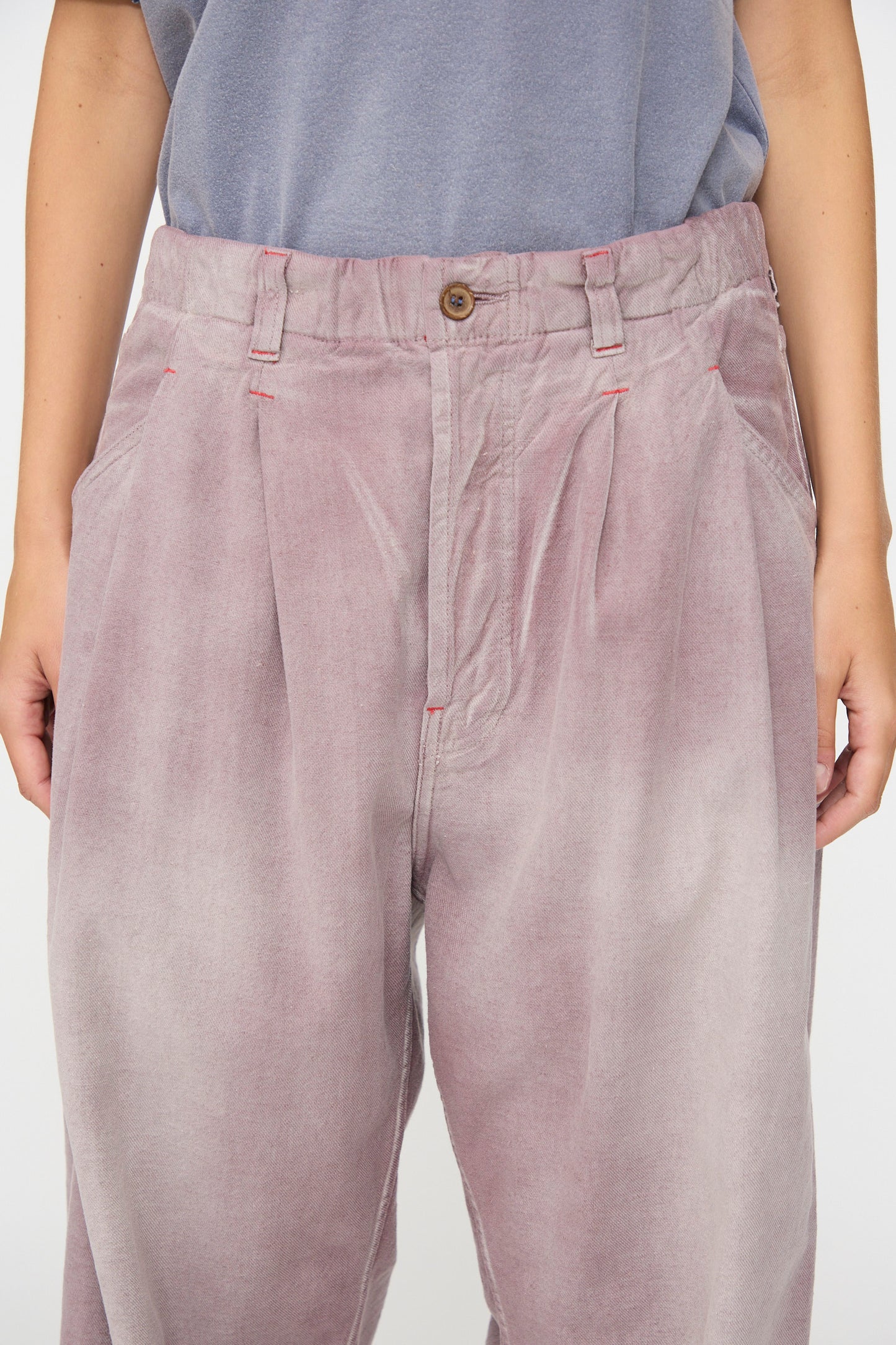 A person is shown from waist to mid-thigh wearing the Dr. Collectors P40 Z Boys Pant in Sunfaded Dusty Orchid—a relaxed, loose-fitting, high-waisted pant featuring pleats and a straight-leg silhouette crafted from soft Japanese cotton—paired with a blue-gray shirt.
