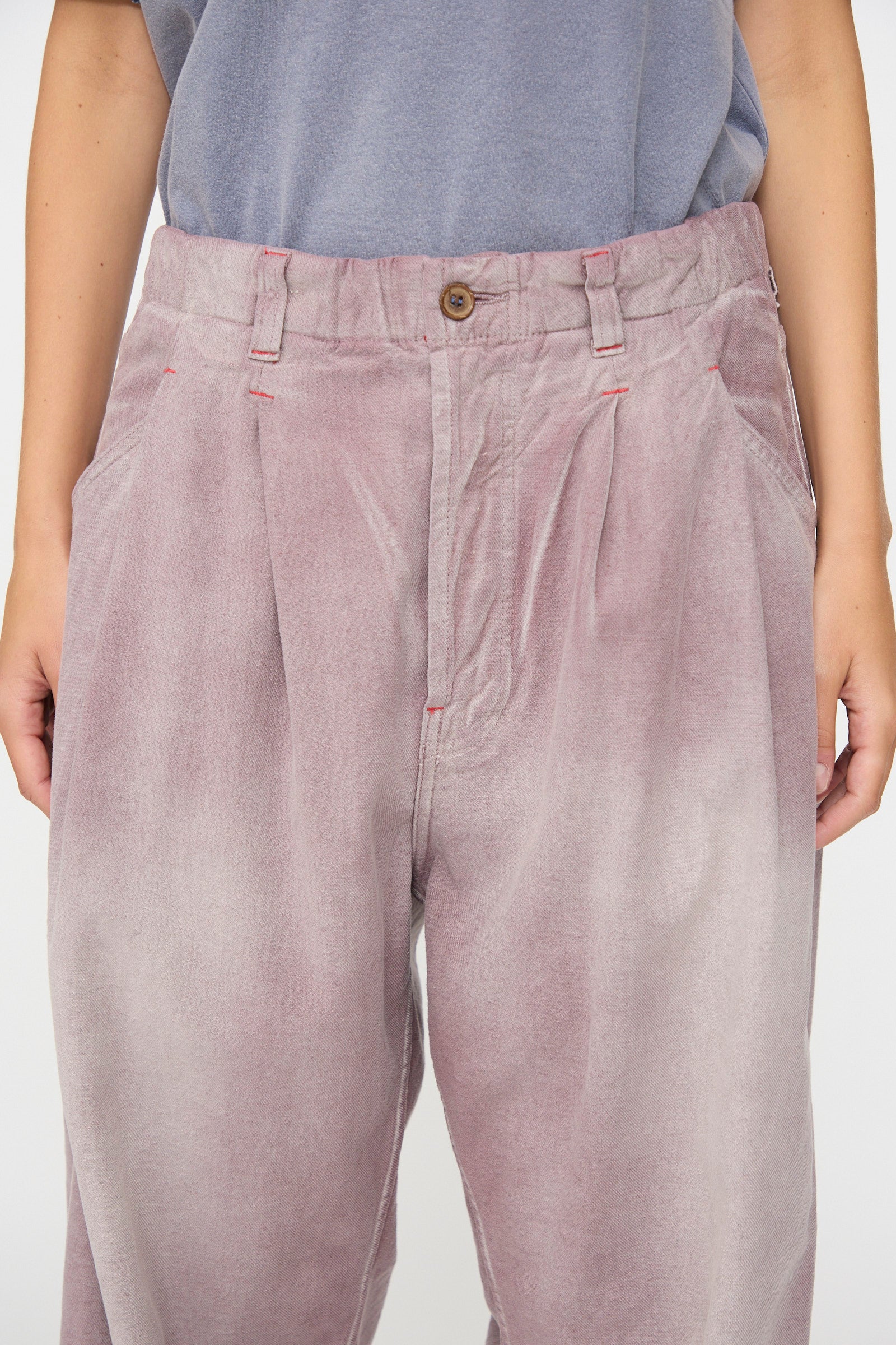 A person is shown from waist to mid-thigh wearing the Dr. Collectors P40 Z Boys Pant in Sunfaded Dusty Orchid—a relaxed, loose-fitting, high-waisted pant featuring pleats and a straight-leg silhouette crafted from soft Japanese cotton—paired with a blue-gray shirt.