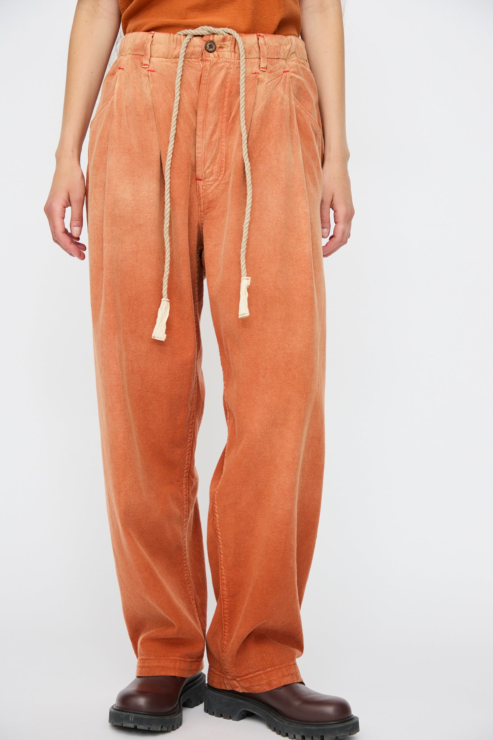 Person wearing Dr. Collectors P40 Z Boys Sunfaded Dye pants in Rust, relaxed fit with elastic waistband, brown boots, and an orange Japanese cotton top; image cropped at the shoulders.