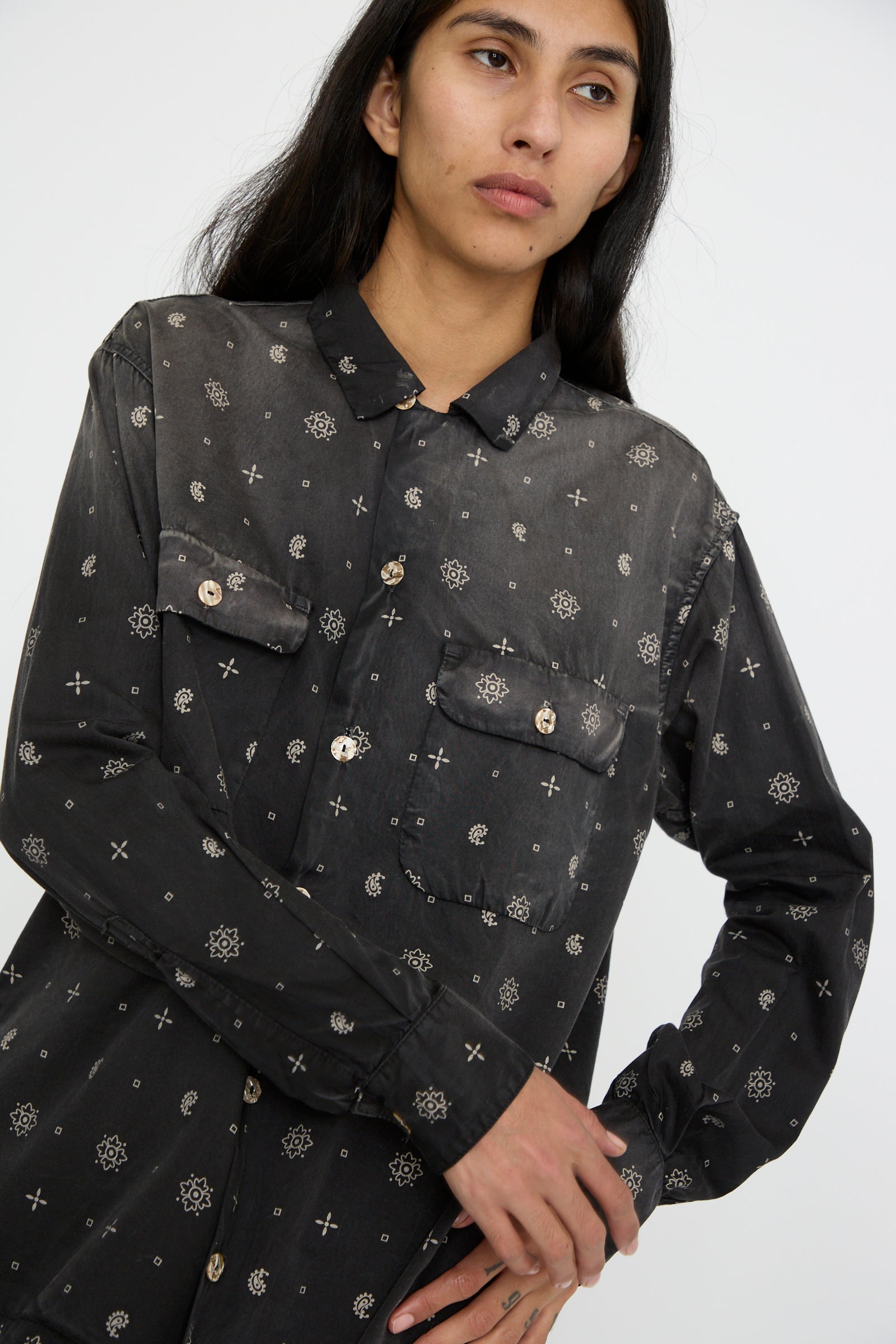 A person stands against a plain background, wearing the Dr. Collectors Sateen Cotton Bowling Long Sleeve in Smoke Black. This stylish shirt features a dark, patterned design with crosses and circles, complemented by abalone shell buttons that catch the light.