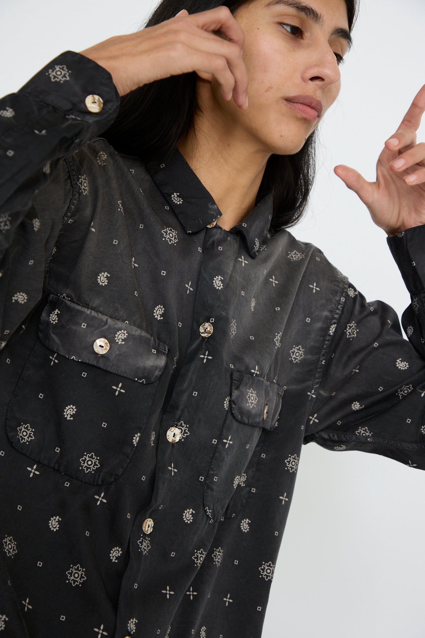 A person wearing the Dr. Collectors Sateen Cotton Bowling Long Sleeve in Smoke Black, adorned with abalone shell buttons, lifts their hands against a plain background.