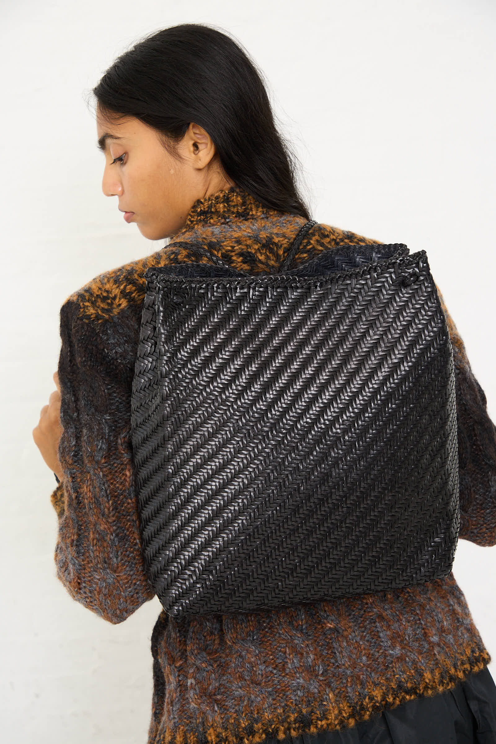 A person with long hair is viewed from the side wearing a textured sweater and carrying a handcrafted **Dragon Diffusion Backpack in Black**.