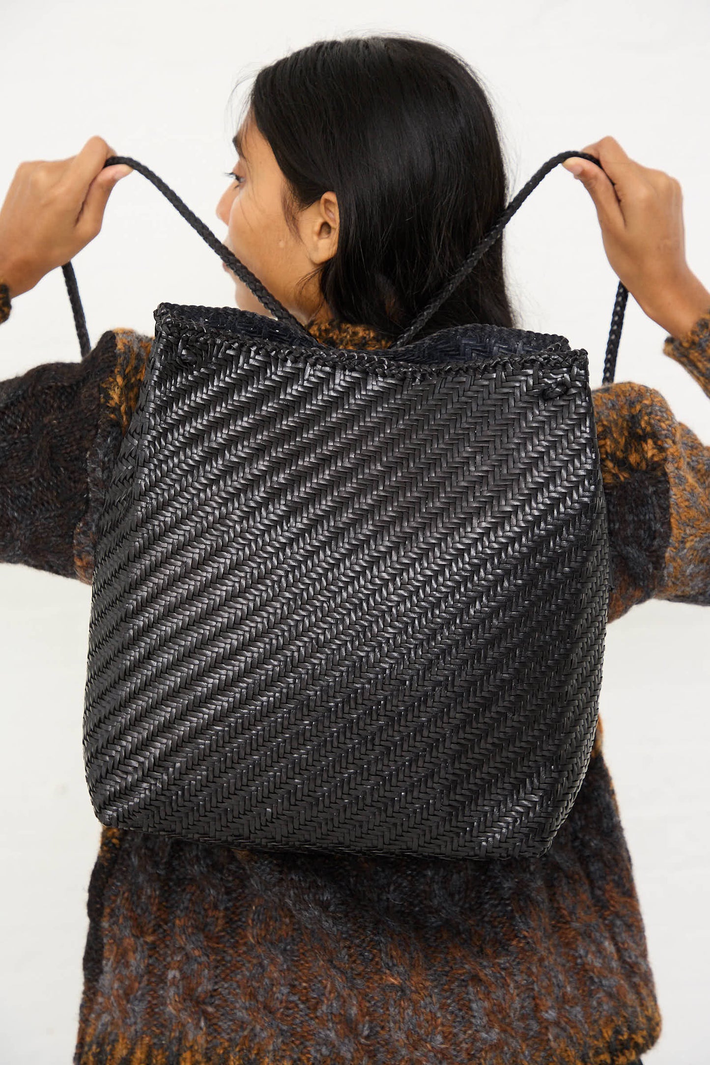 A person with long black hair holds the intricately woven, handcrafted Dragons Diffusion Backpack in Black over their shoulders, facing away from the camera.