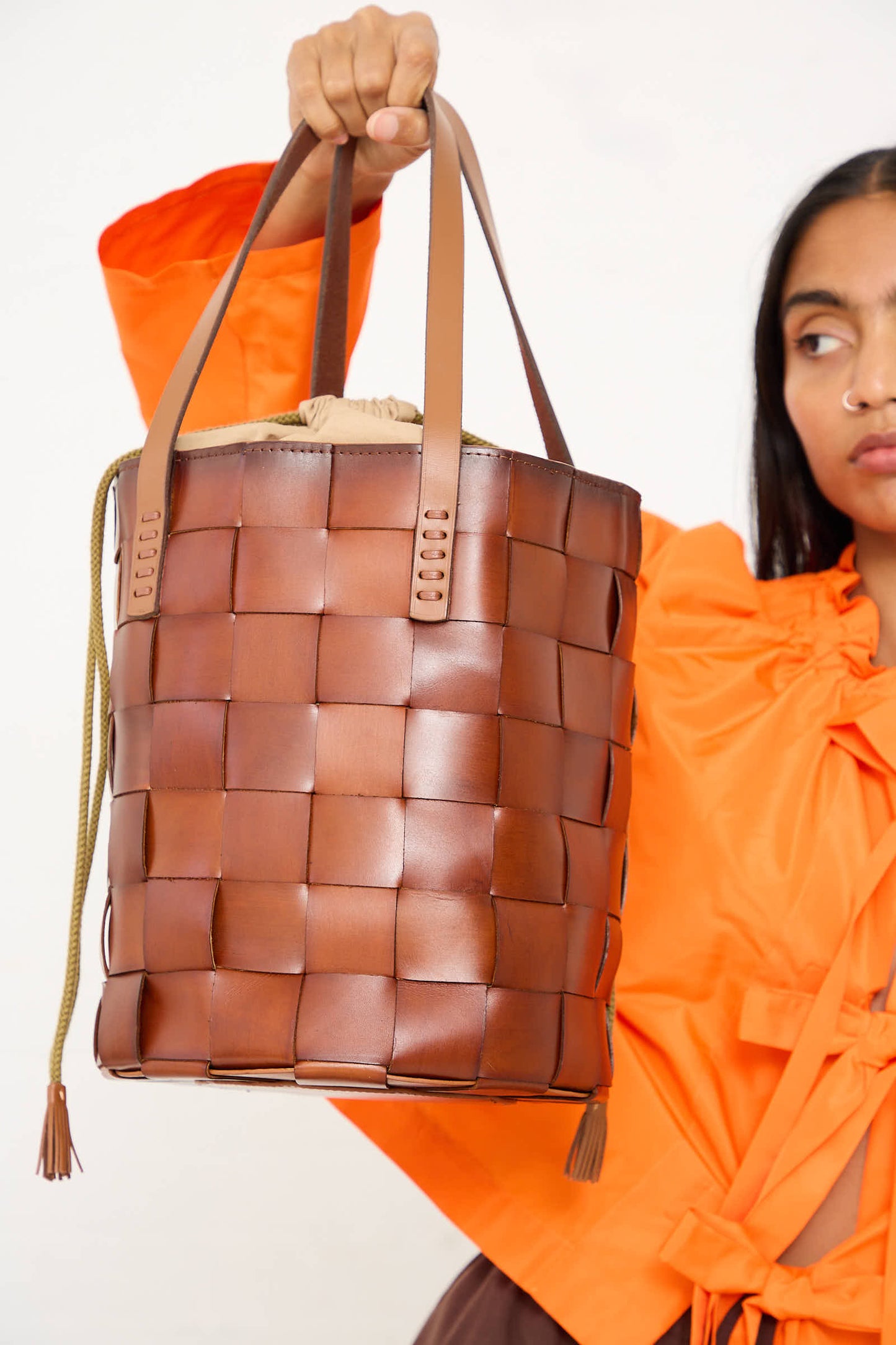 A person in an orange top holds the Dragon Diffusion Box Weave Japan Bucket in Tan, showcasing traditional weaving techniques.