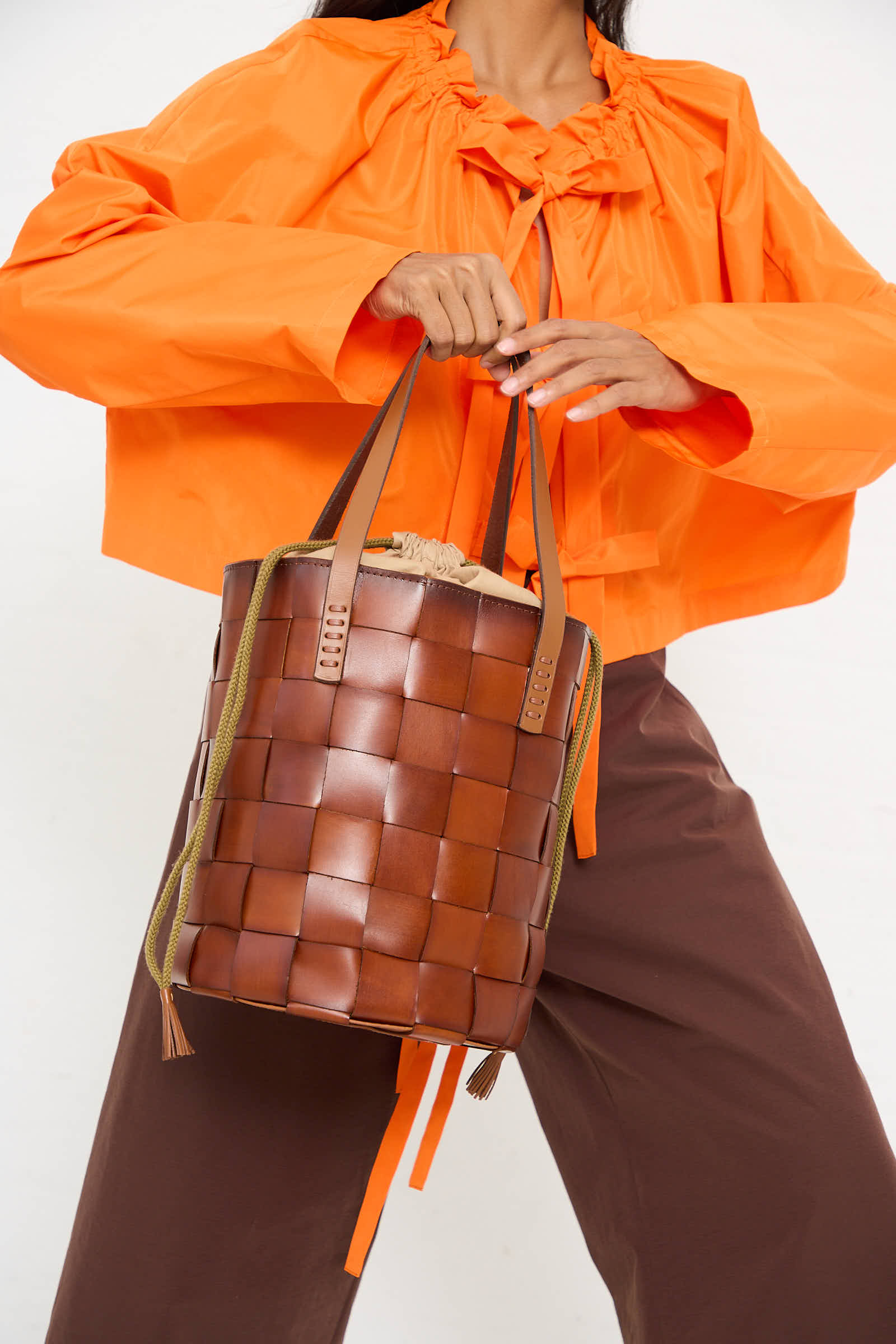 Person wearing an orange top and brown pants holds the Dragon Diffusion Box Weave Japan Bucket in Tan, crafted with traditional weaving techniques.