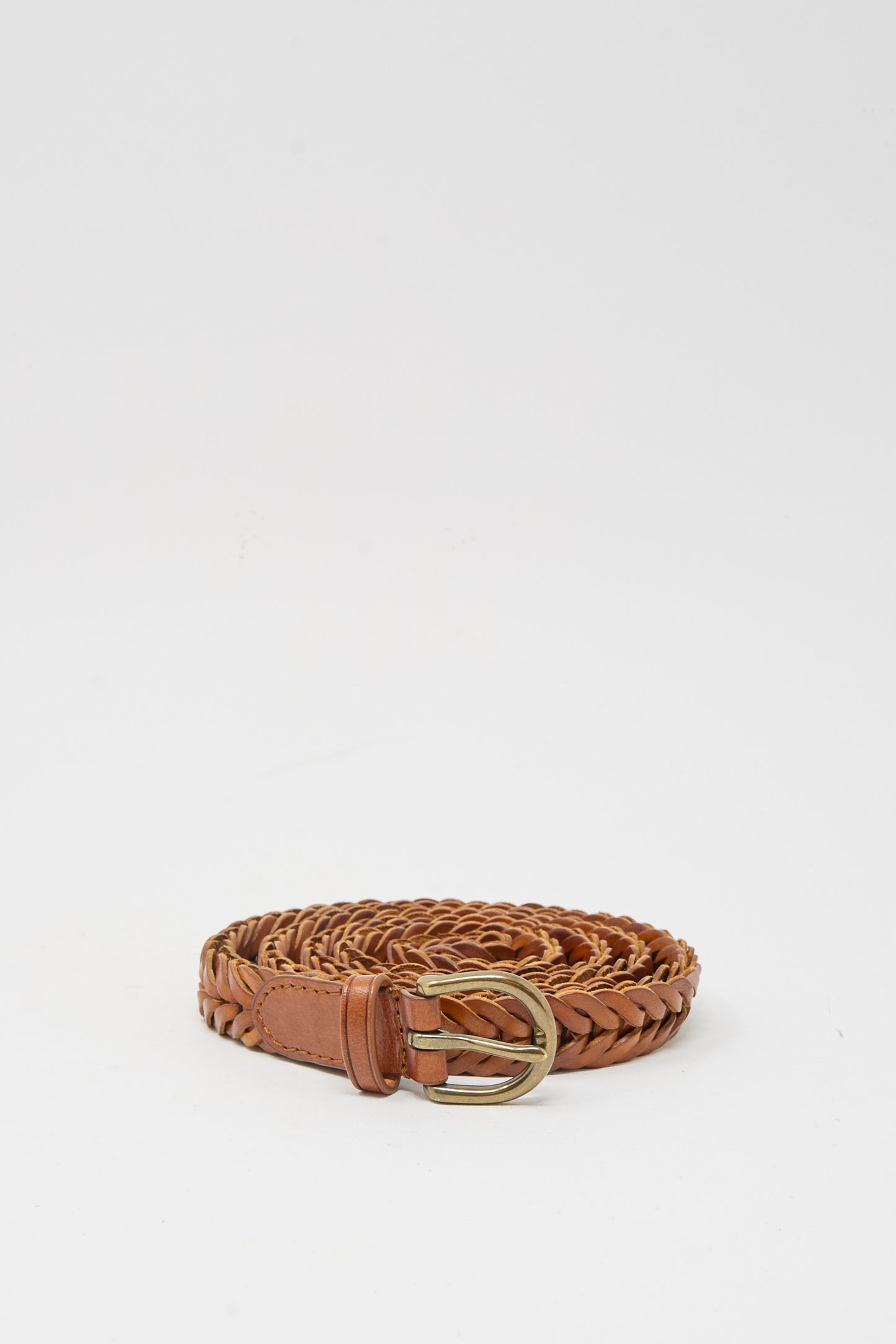The Brass Buckle Single Link Belt in Tan by Dragon Diffusion, featuring a brass buckle and handcrafted braided leather, is displayed rolled up on a plain white background.