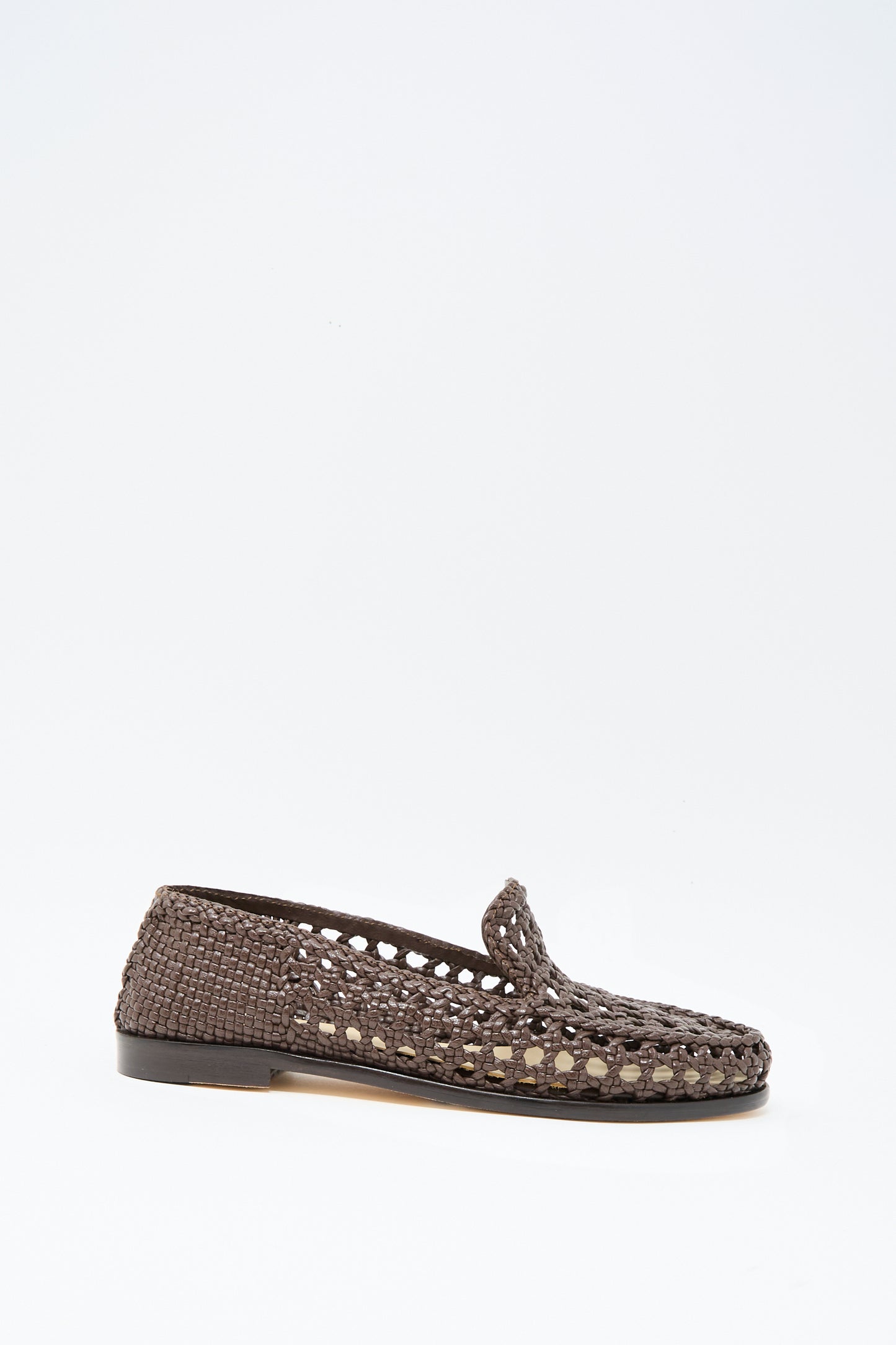 The Dolly Moccasin in Dark Brown by Dragon Diffusion is a woven leather slip-on with an almond toe and flat black sole, shown against a plain white background.