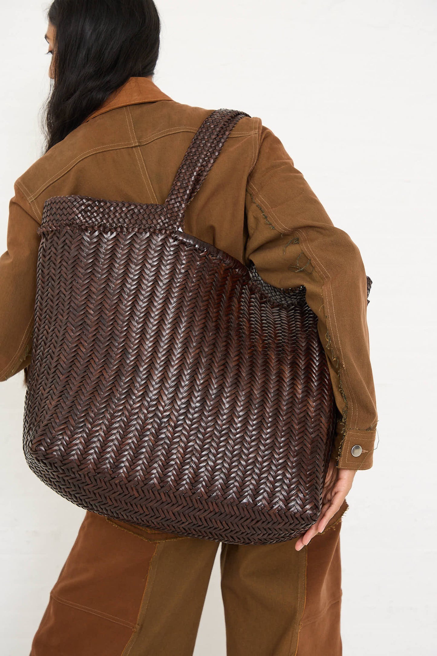 A person wearing a brown jacket carries Dragon Diffusion's Oversize Triple Jump Weave Maxi Shopper in Dark Brown over their shoulder.