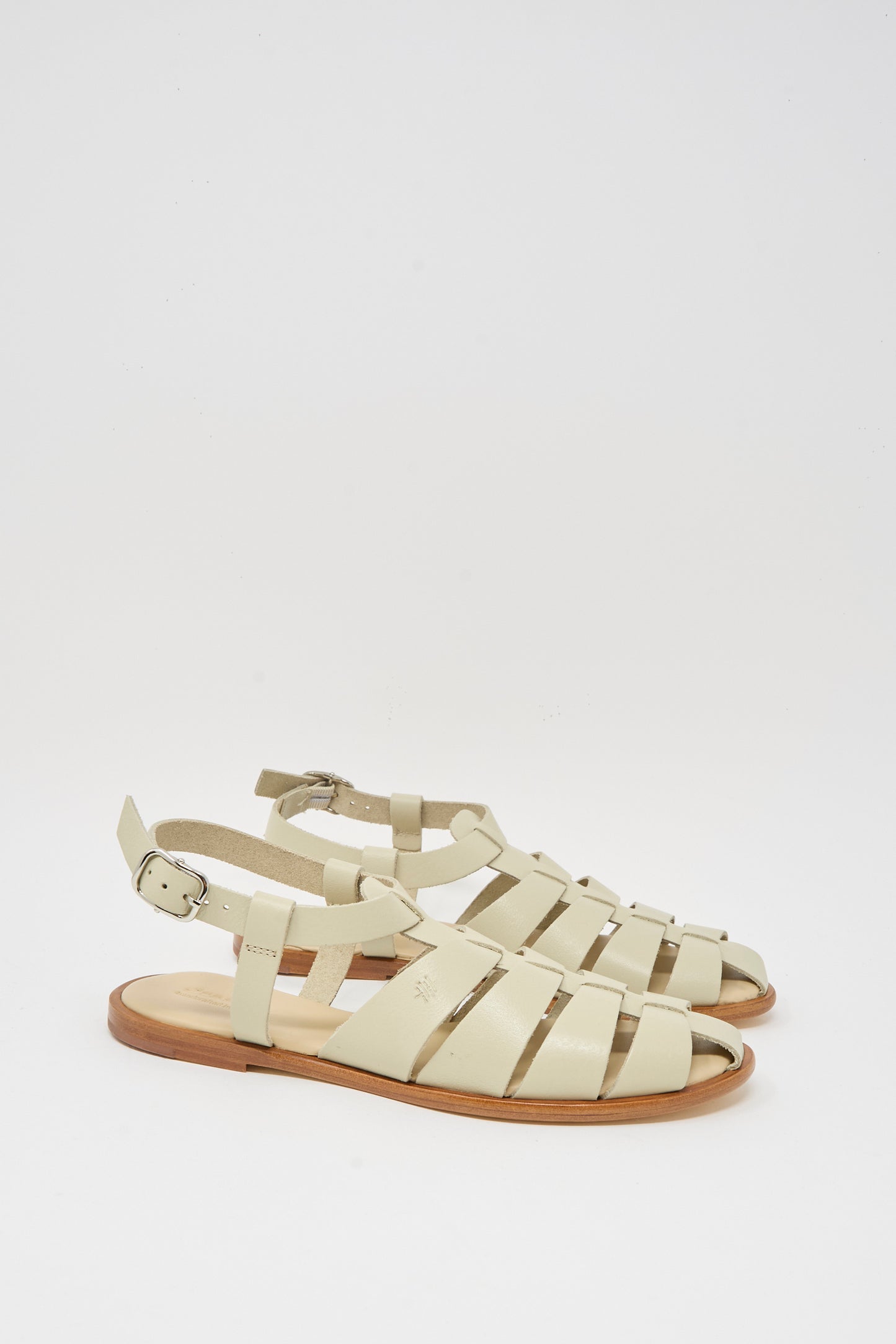 The Pescador Sandal in Pearl by Dragon Diffusion features handcrafted beige cow leather with closed toes, ankle straps, silver buckles, and flat wooden soles, shown against a plain white background.