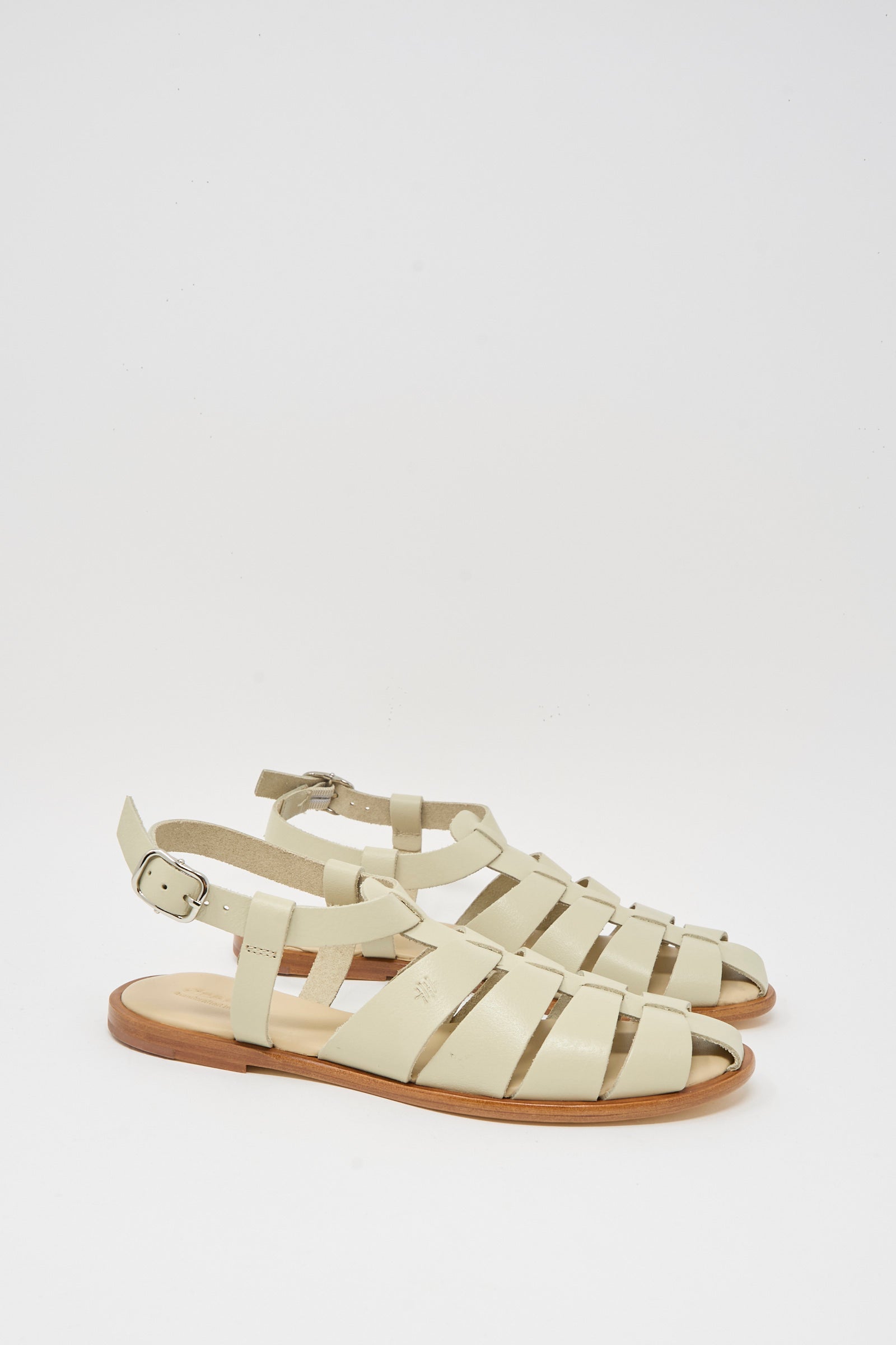 The Pescador Sandal in Pearl by Dragon Diffusion features handcrafted beige cow leather with closed toes, ankle straps, silver buckles, and flat wooden soles, shown against a plain white background.