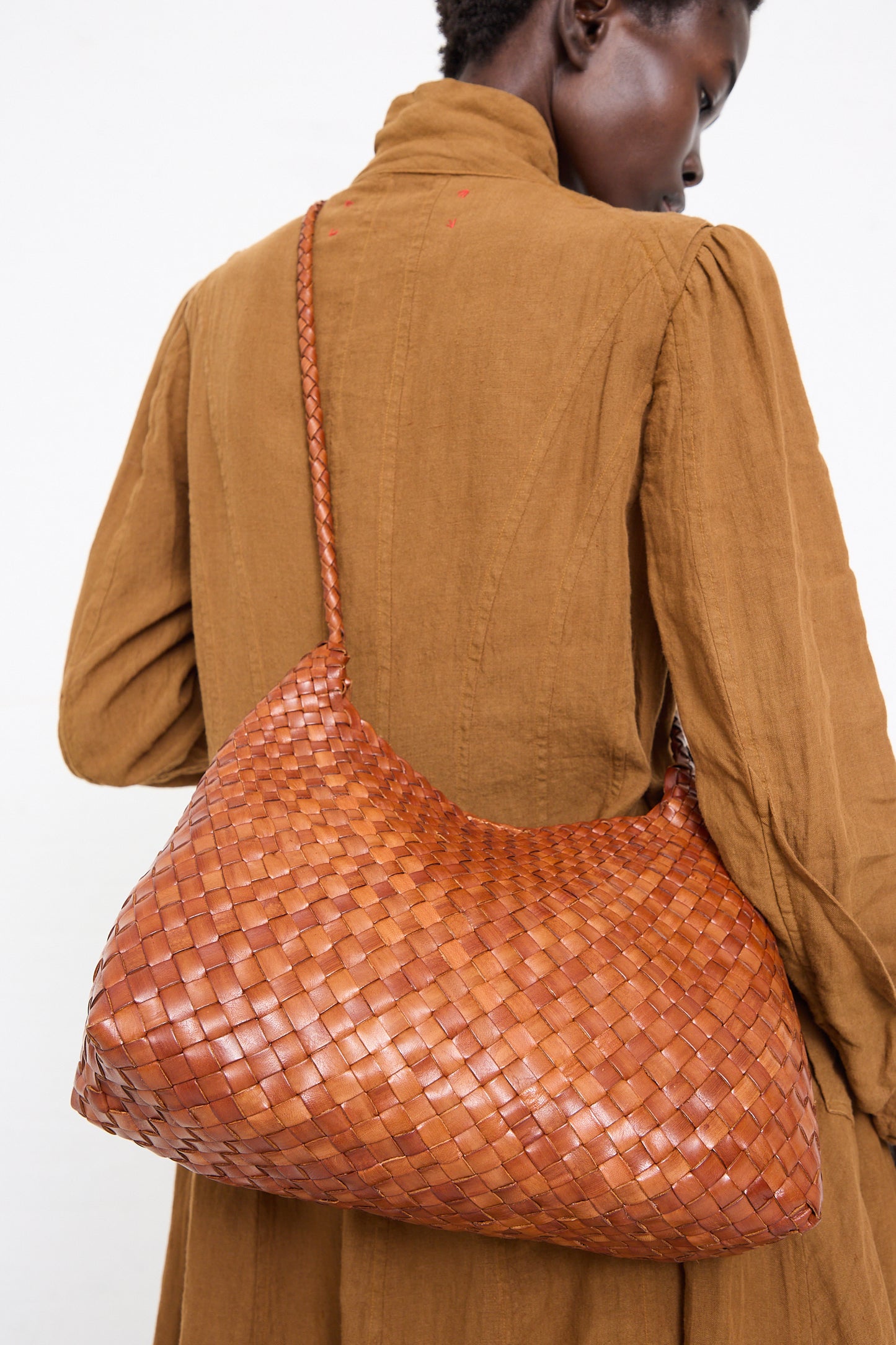 Person from behind wearing a beige jacket with a textured, oversized Dragon Diffusion Santa Rosa in Tan shoulder bag over their shoulder.
