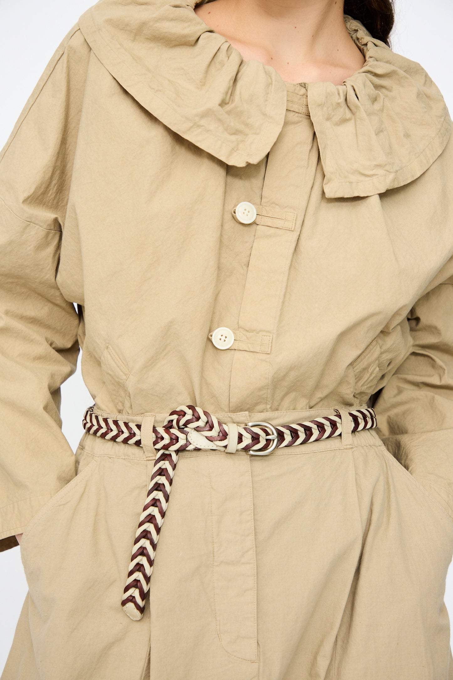 A person wearing a beige coat with a wide collar and three buttons, cinched at the waist with Dragon Diffusion’s Single Link Bi-Color Belt in Bruciato and Pearl, showcasing traditional craftsmanship.