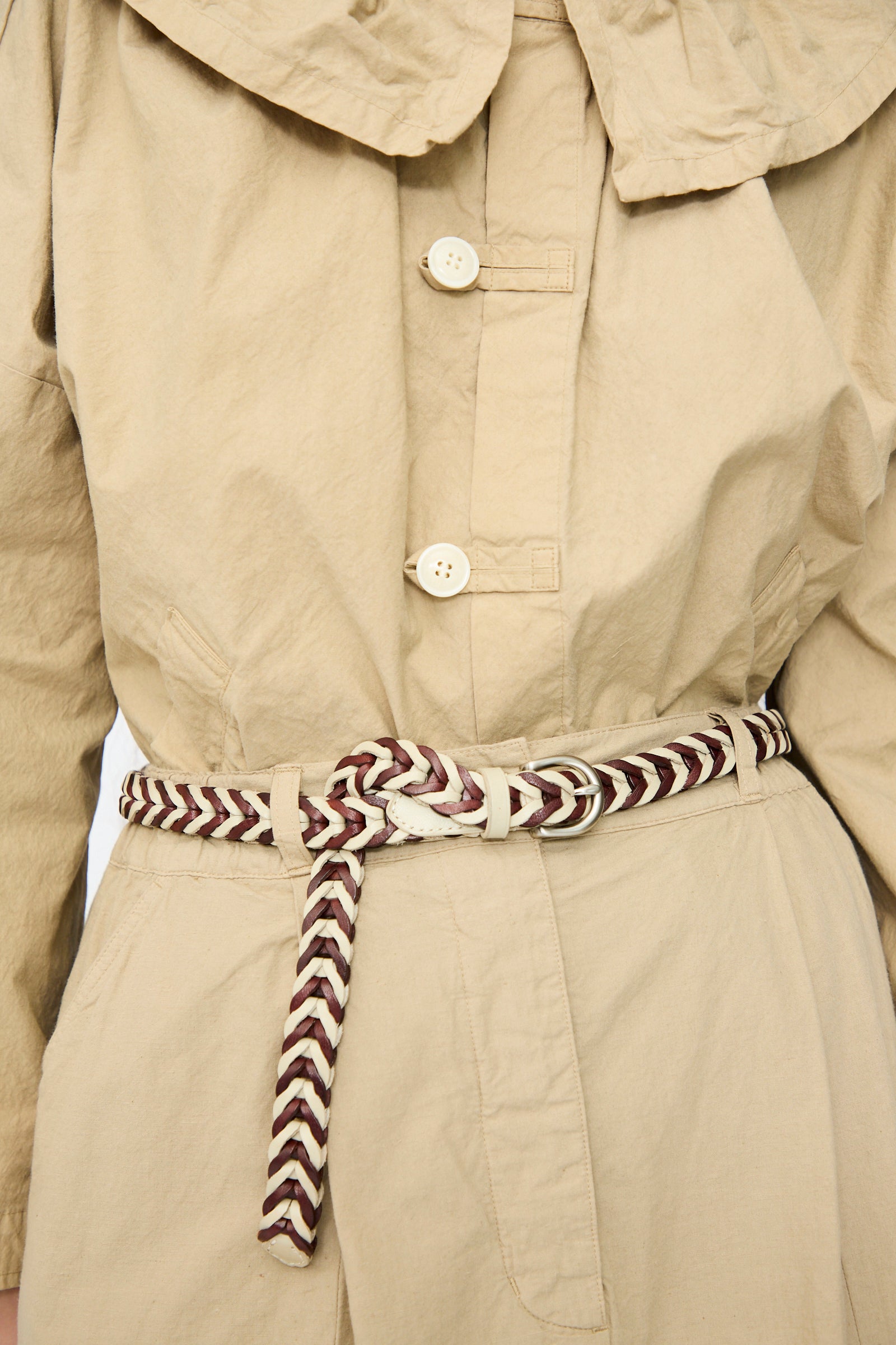 Close-up of a beige trench coat featuring Dragon Diffusion's Single Link Bi-Color Belt in Bruciato and Pearl, tied at the waist to highlight its traditional weaving techniques in cream and brown leather.
