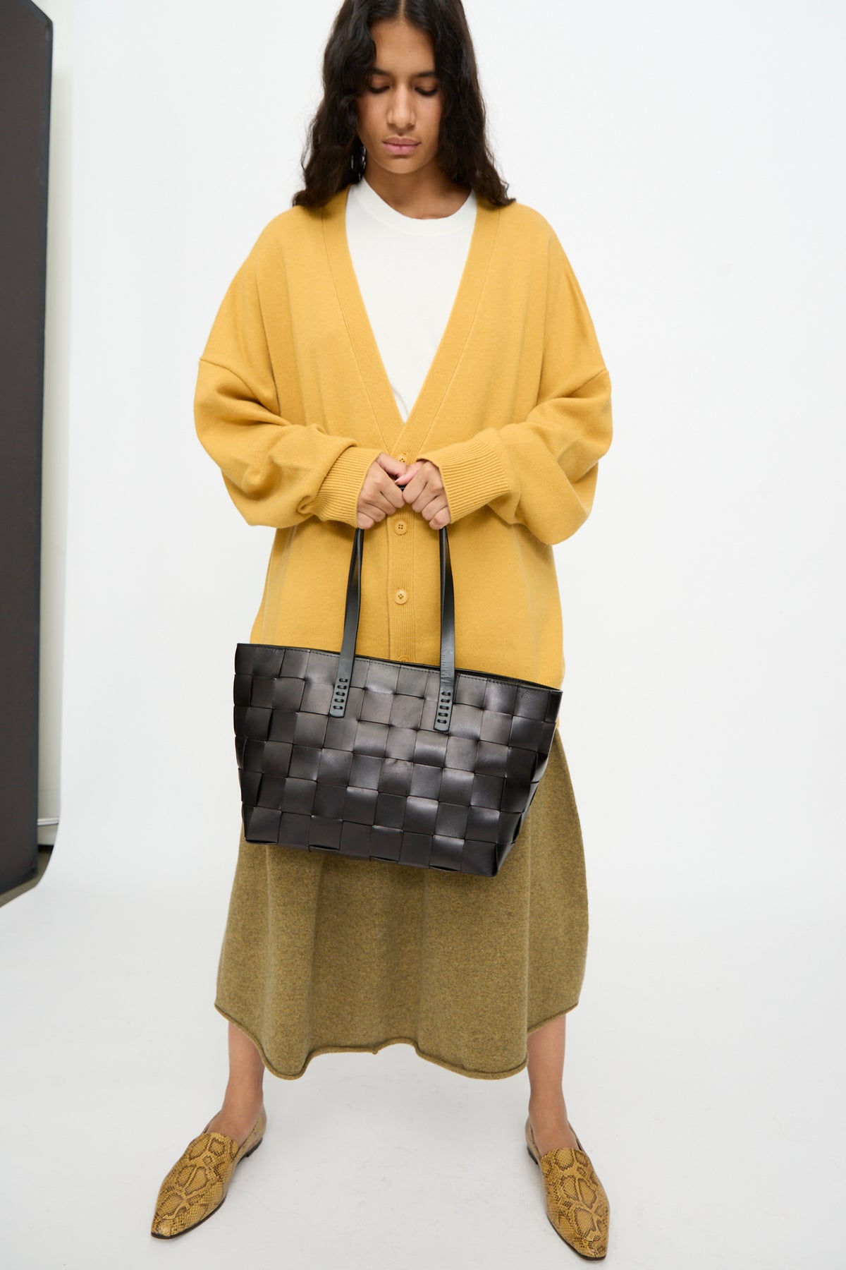 A person wearing a yellow cardigan, white shirt, and olive skirt stands holding the Dragon Diffusion Japan Tote in Black.