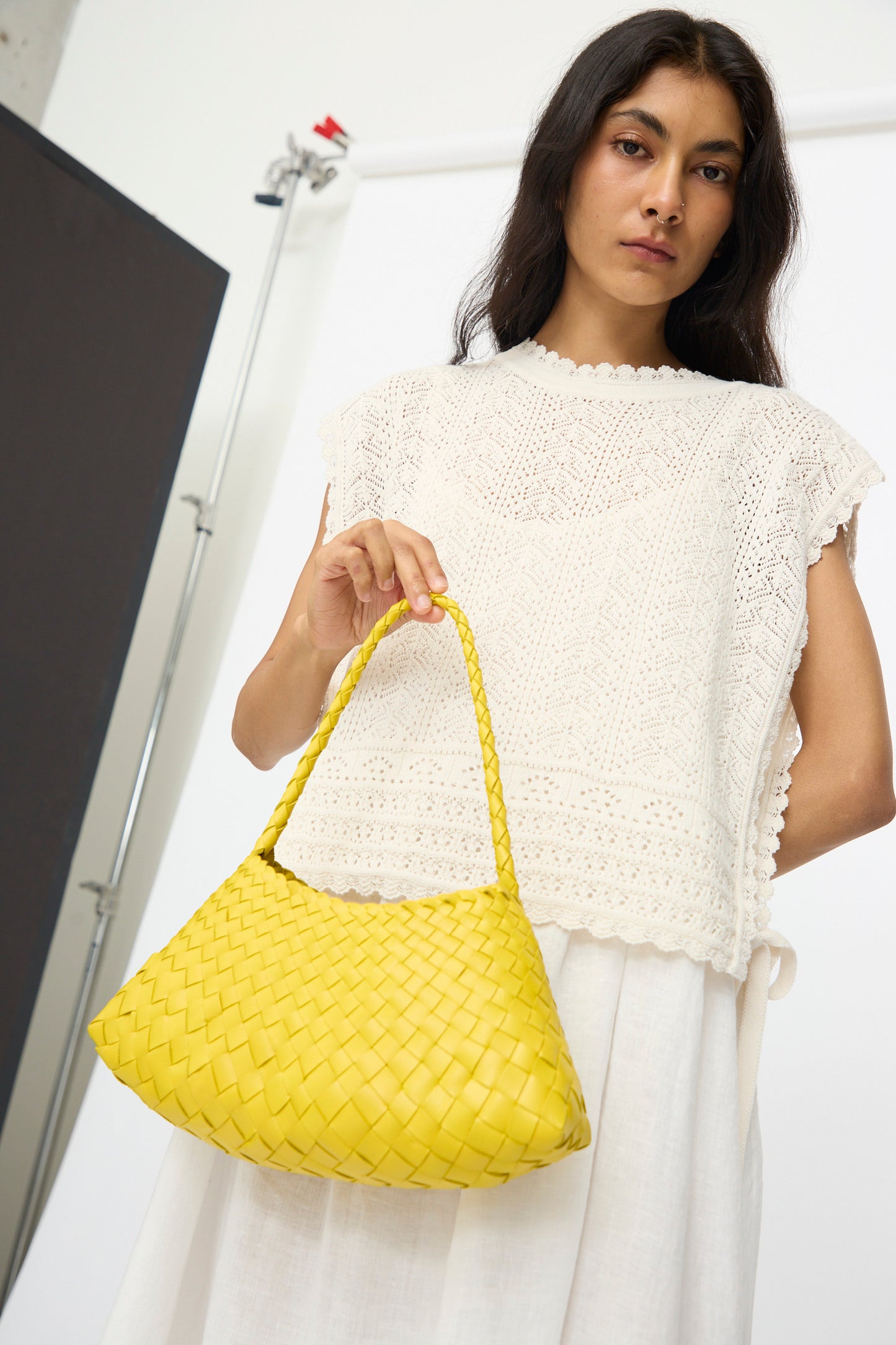 A woman in a white lace top holds the Dragon Diffusion Rosanna Bag in Yellow, standing before a white studio backdrop.