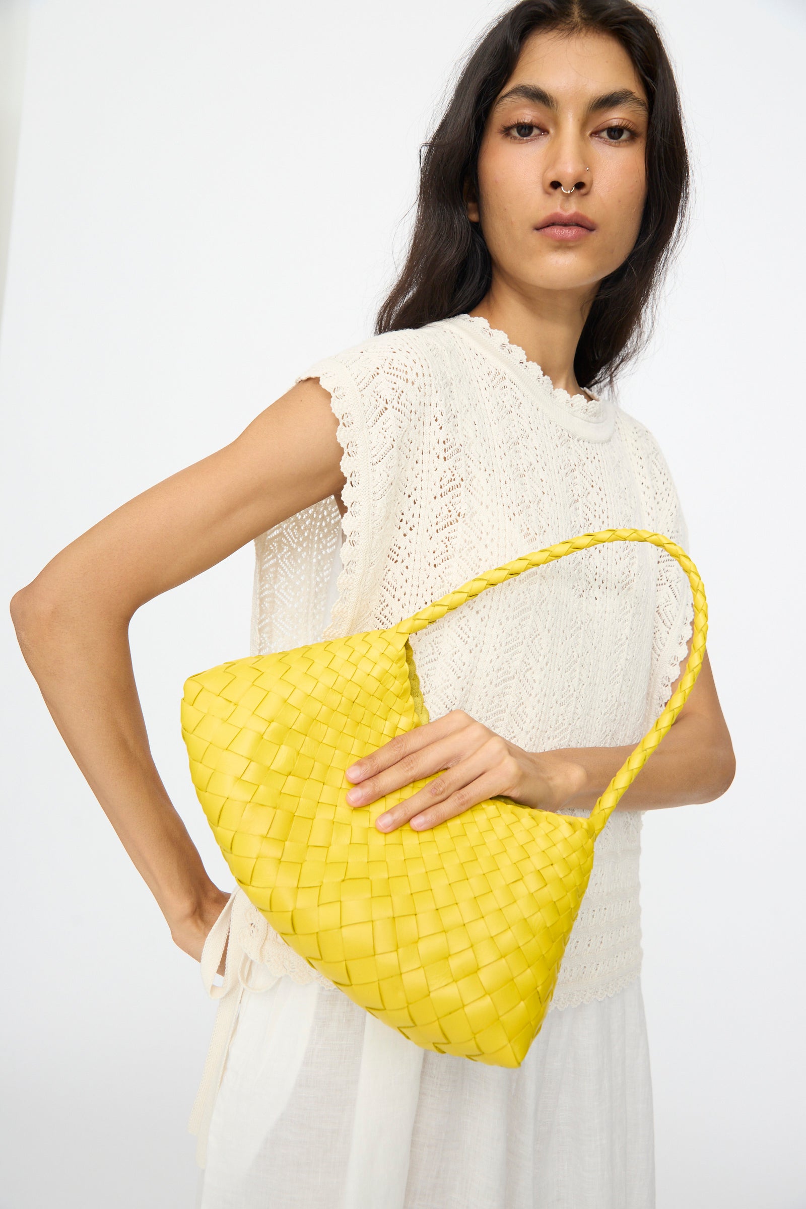 A woman in a white sleeveless top holds the Rosanna Bag in Yellow by Dragon Diffusion under her arm, standing against a plain light background.