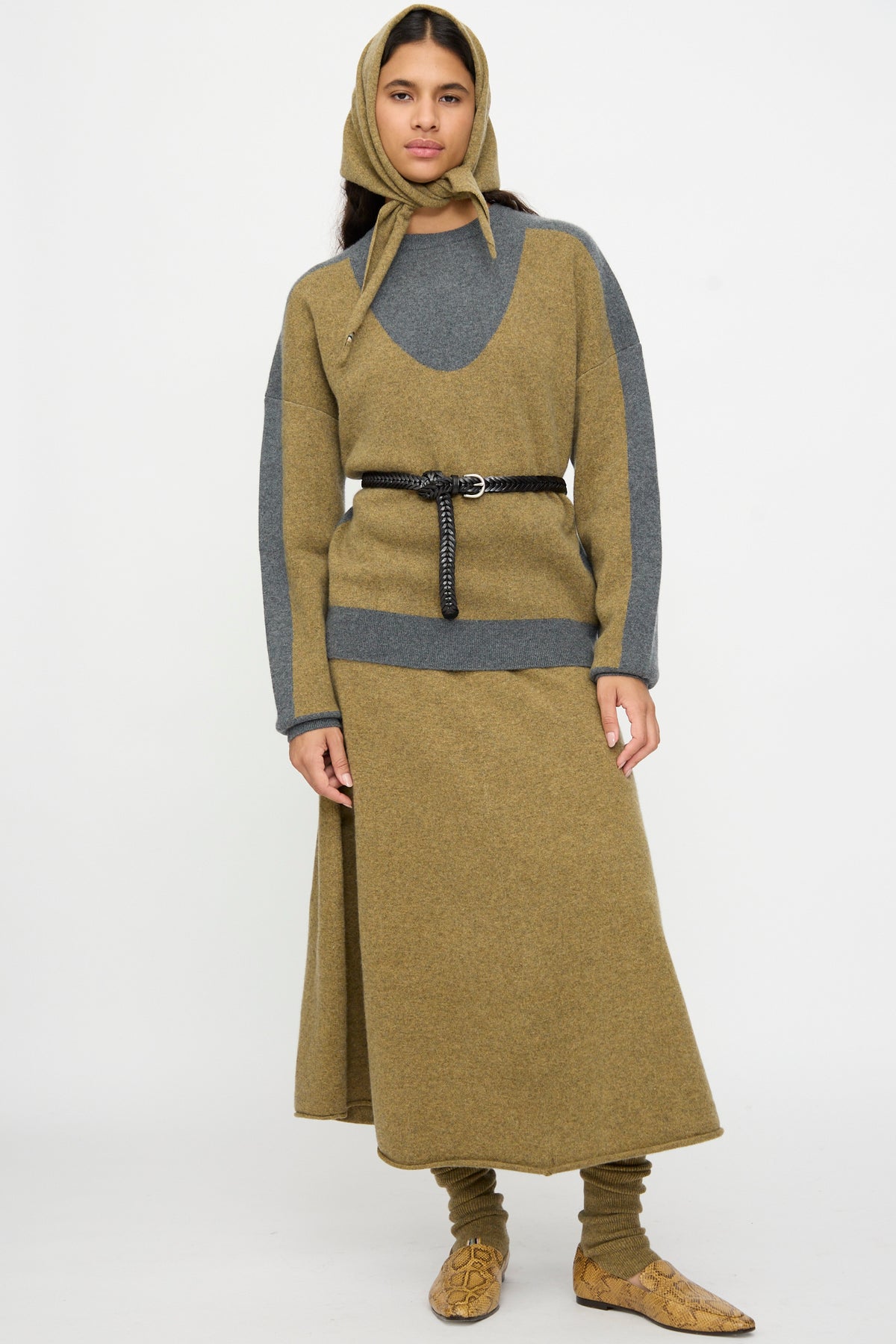 A person stands facing forward against a plain white background, wearing a tan and gray knit outfit with a matching headscarf, long skirt, patterned shoes, and the Dragon Diffusion Single Link Belt in Black at the waist.