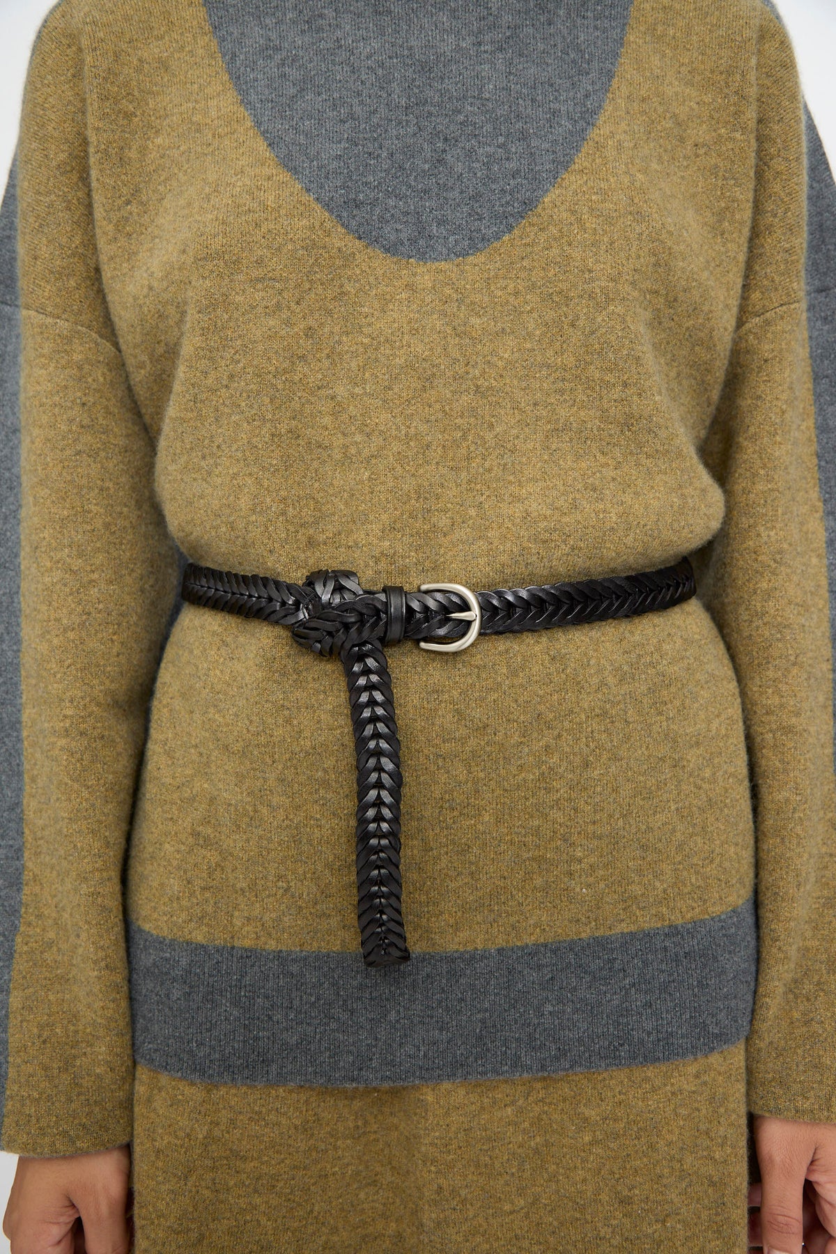 A person wearing a color-blocked sweater in olive and gray, cinched at the waist with the Dragon Diffusion Single Link Belt in Black, tied at the front.