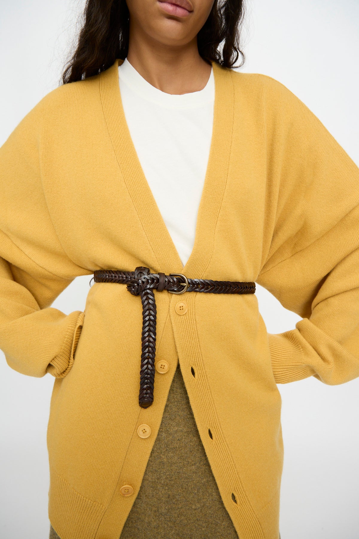 A person wears a mustard yellow cardigan over a white shirt, cinched at the waist with the Dragon Diffusion Single Link Belt in Brown.