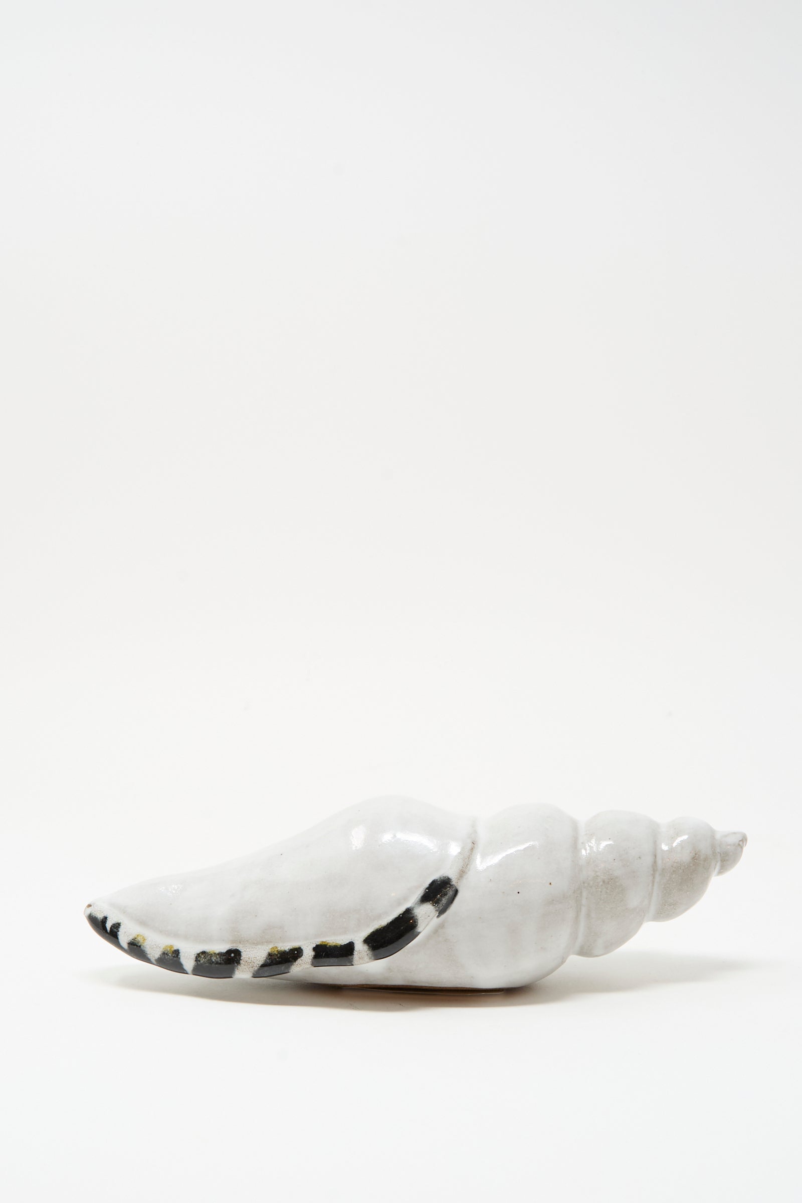 The Shell Rattle LXXXII by E.C.C.E is a handmade ceramic conch sculpture from NYC, featuring white with black markings and shown against a plain white background.