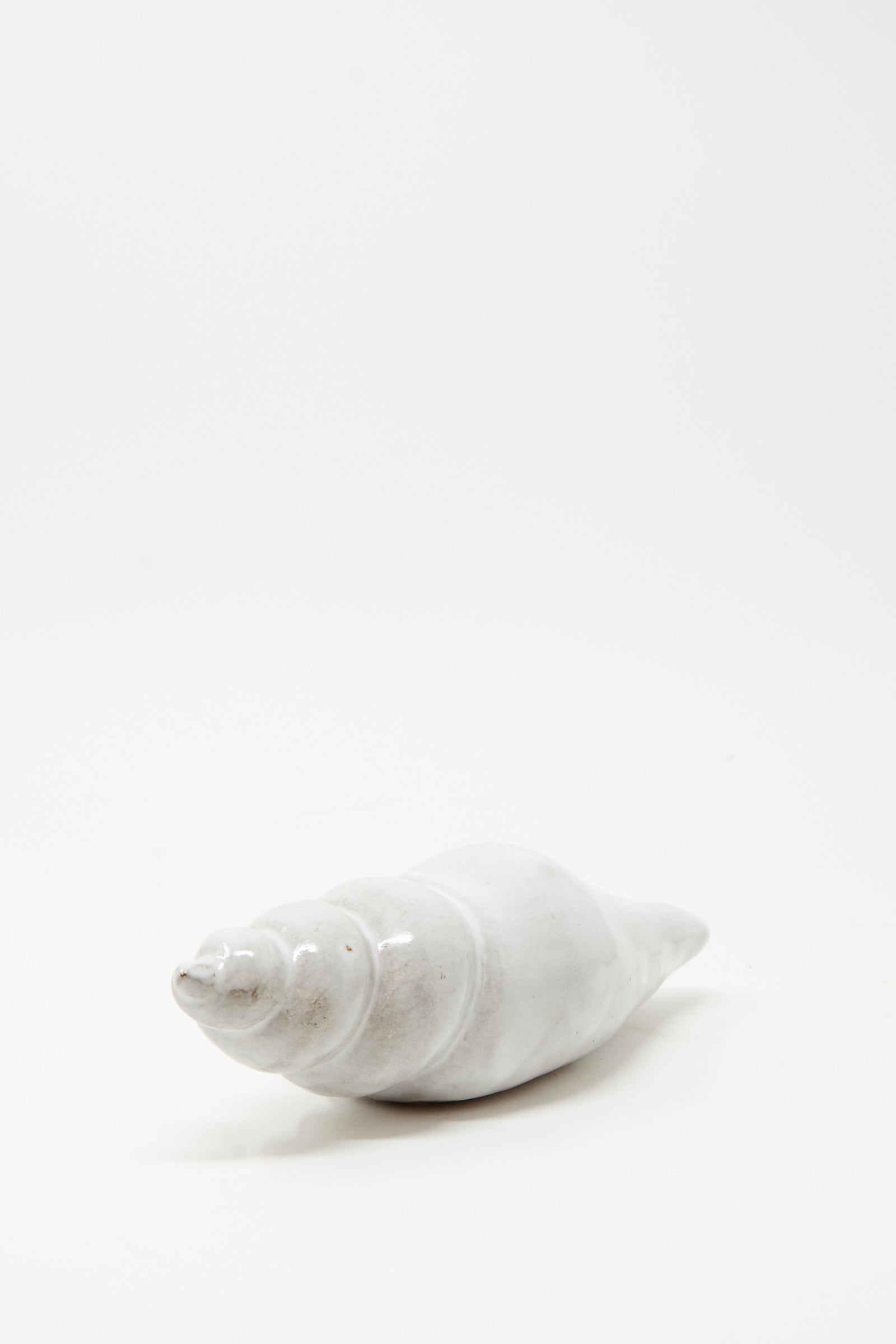 The Shell Rattle LXXXII by E.C.C.E, a handmade ceramic piece crafted in NYC, rests on a plain white surface with a minimalistic background, creating an atmosphere of tranquility.