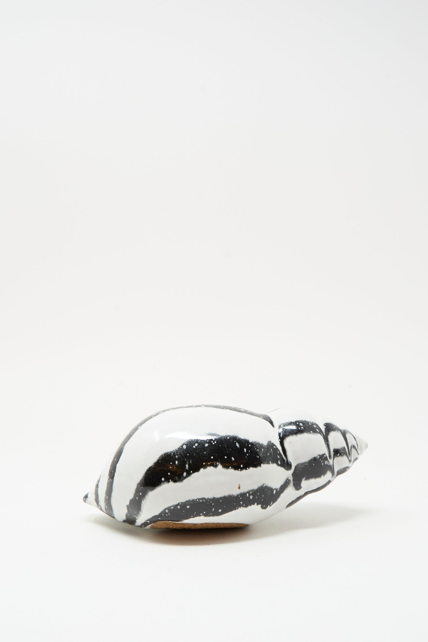 The Shell Rattle LXXXV by E.C.C.E, a handmade black and white striped ceramic piece from NYC, rests on a plain white surface.