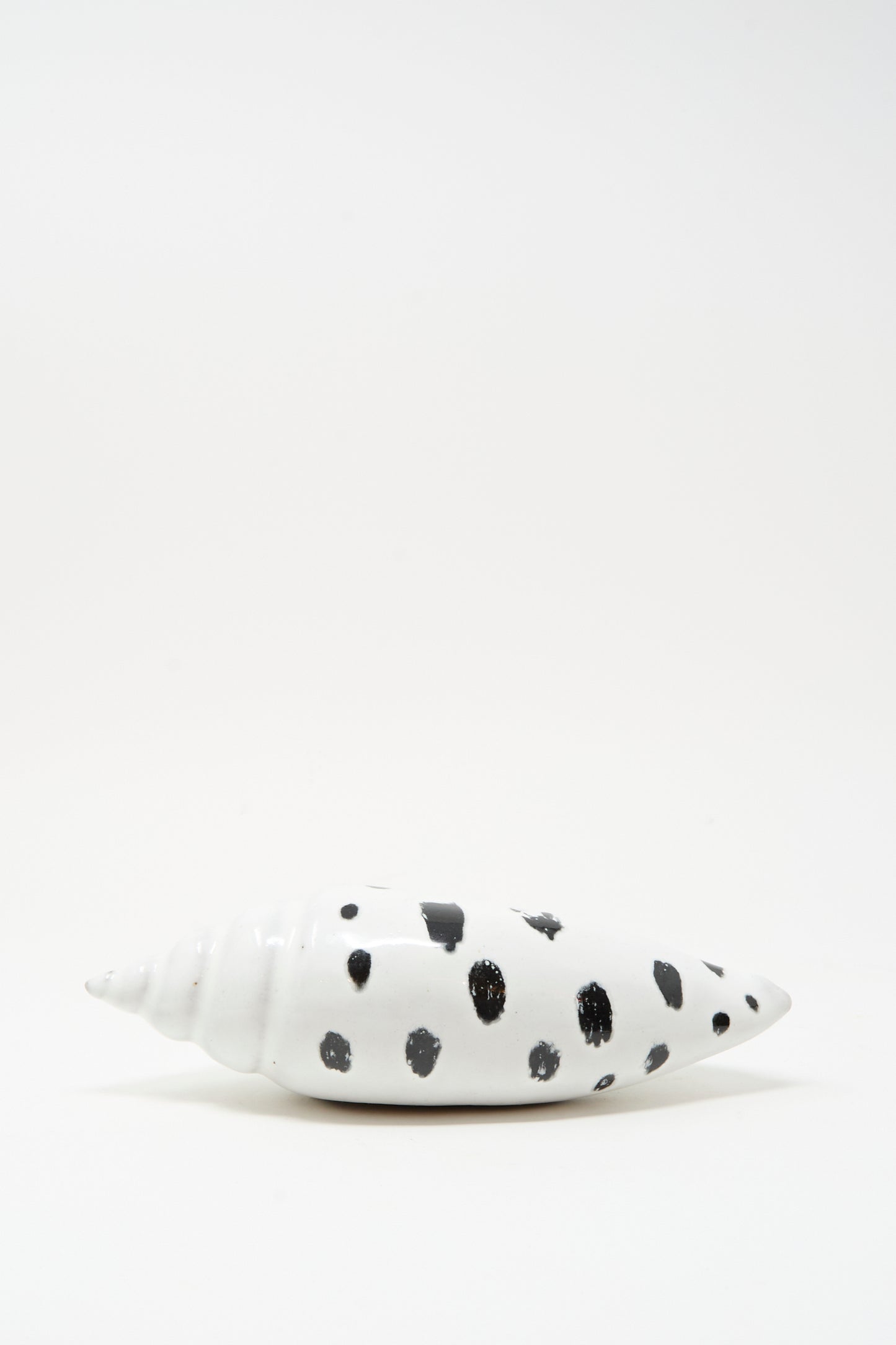 The E.C.C.E Shell Rattle XCIII, a handmade ceramic piece with black spots, is displayed on a plain white surface with a white background.
