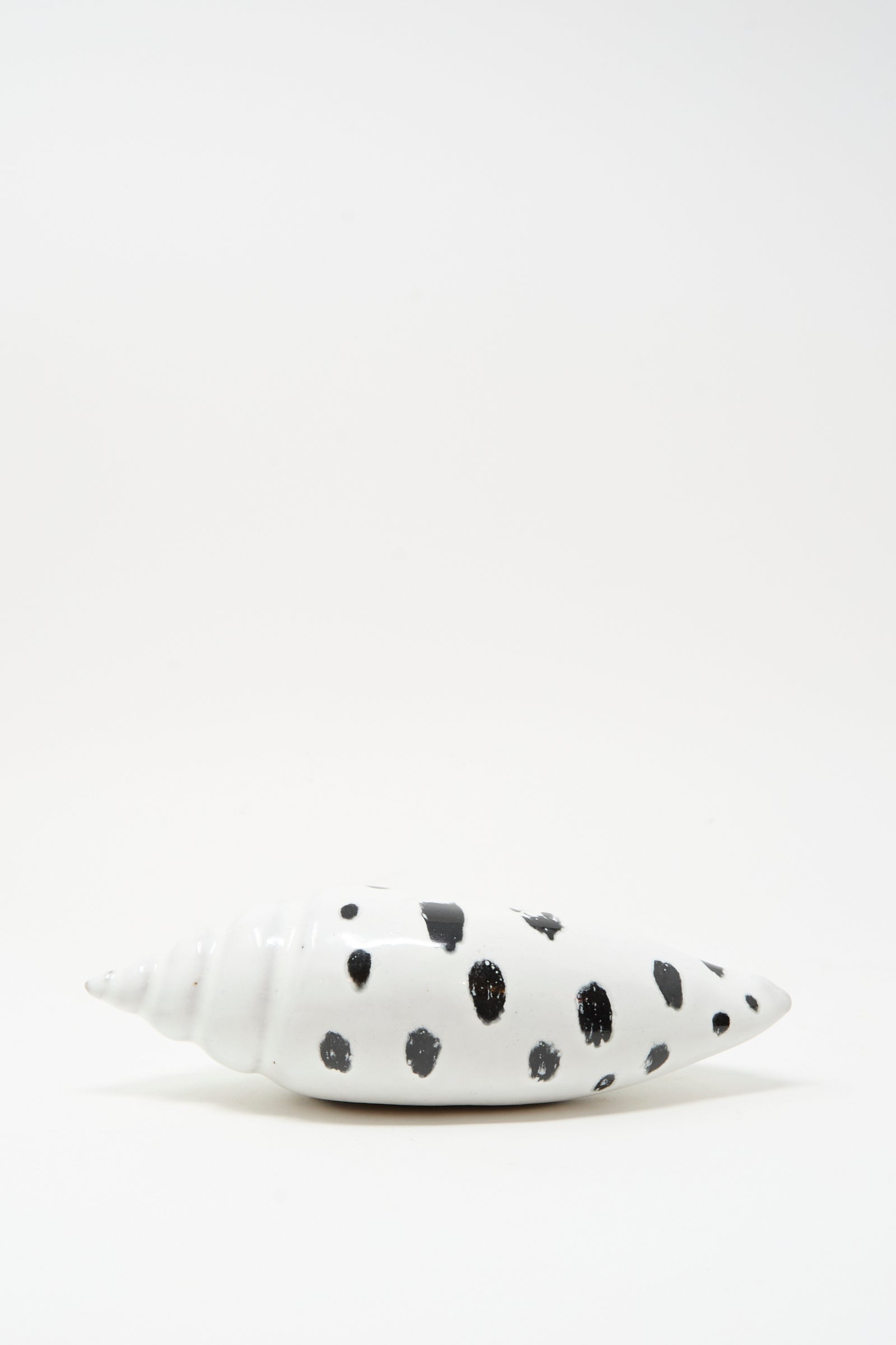 The E.C.C.E Shell Rattle XCIII, a handmade ceramic piece with black spots, is displayed on a plain white surface with a white background.