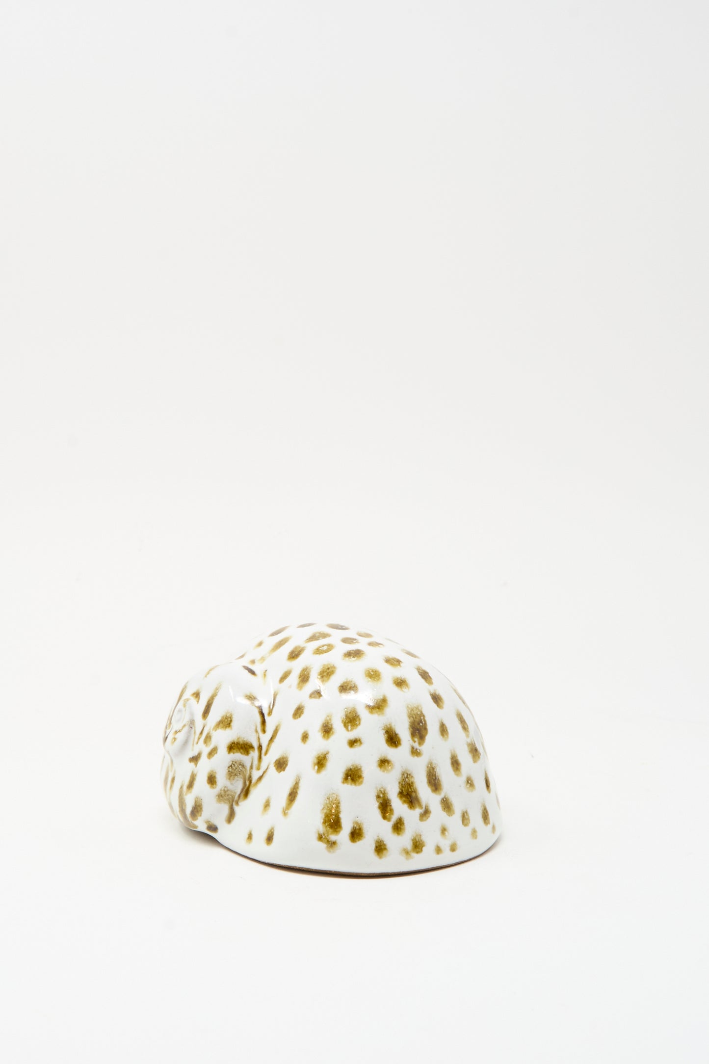 The Shell Rattle XCIV by E.C.C.E is a small, handmade white ceramic piece with brown spots, shaped like a curled-up animal, crafted in NYC and displayed on a plain white background.