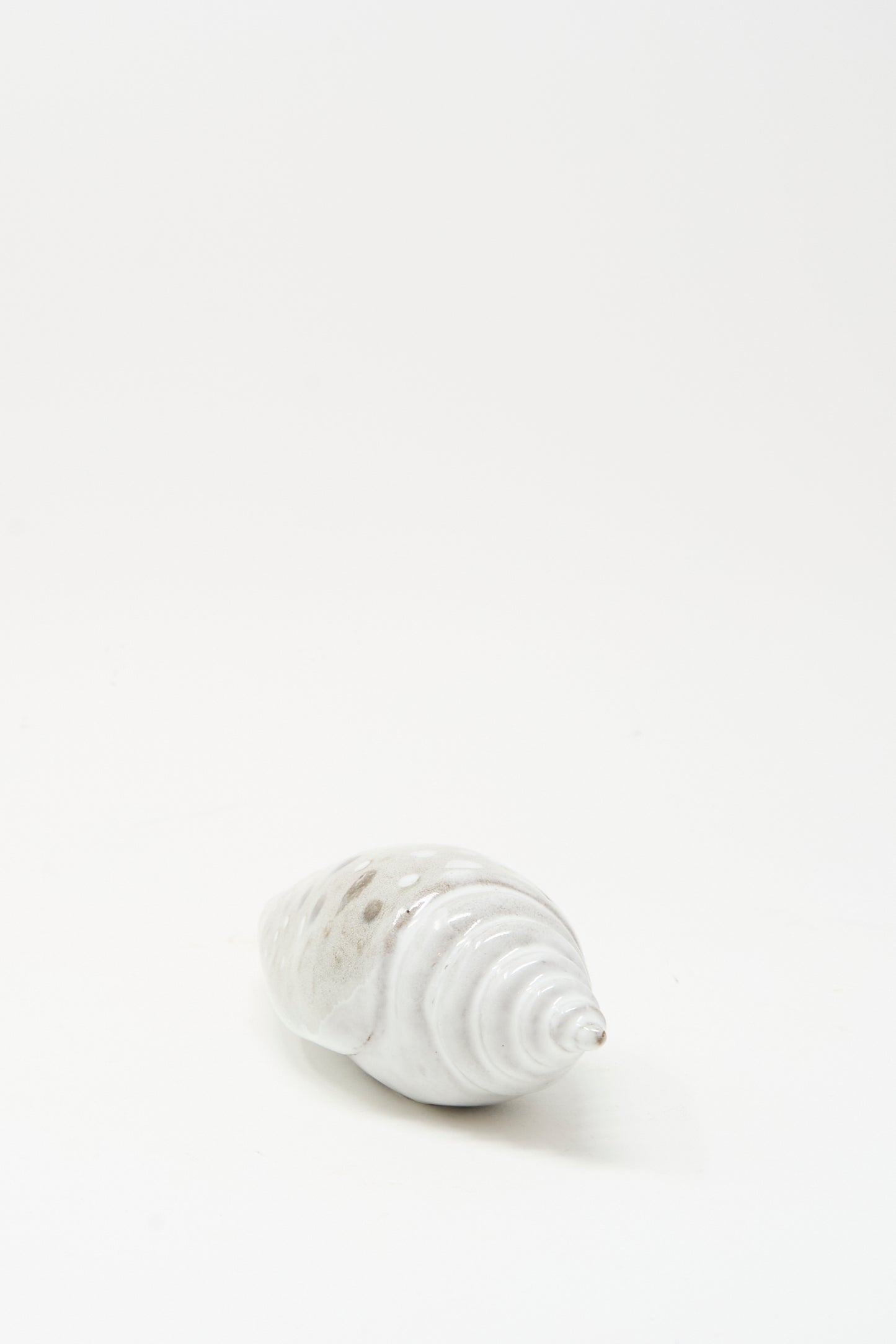 The E.C.C.E Shell Rattle XCV, a handmade white ceramic piece with subtle brown spots, is displayed on a plain white background.