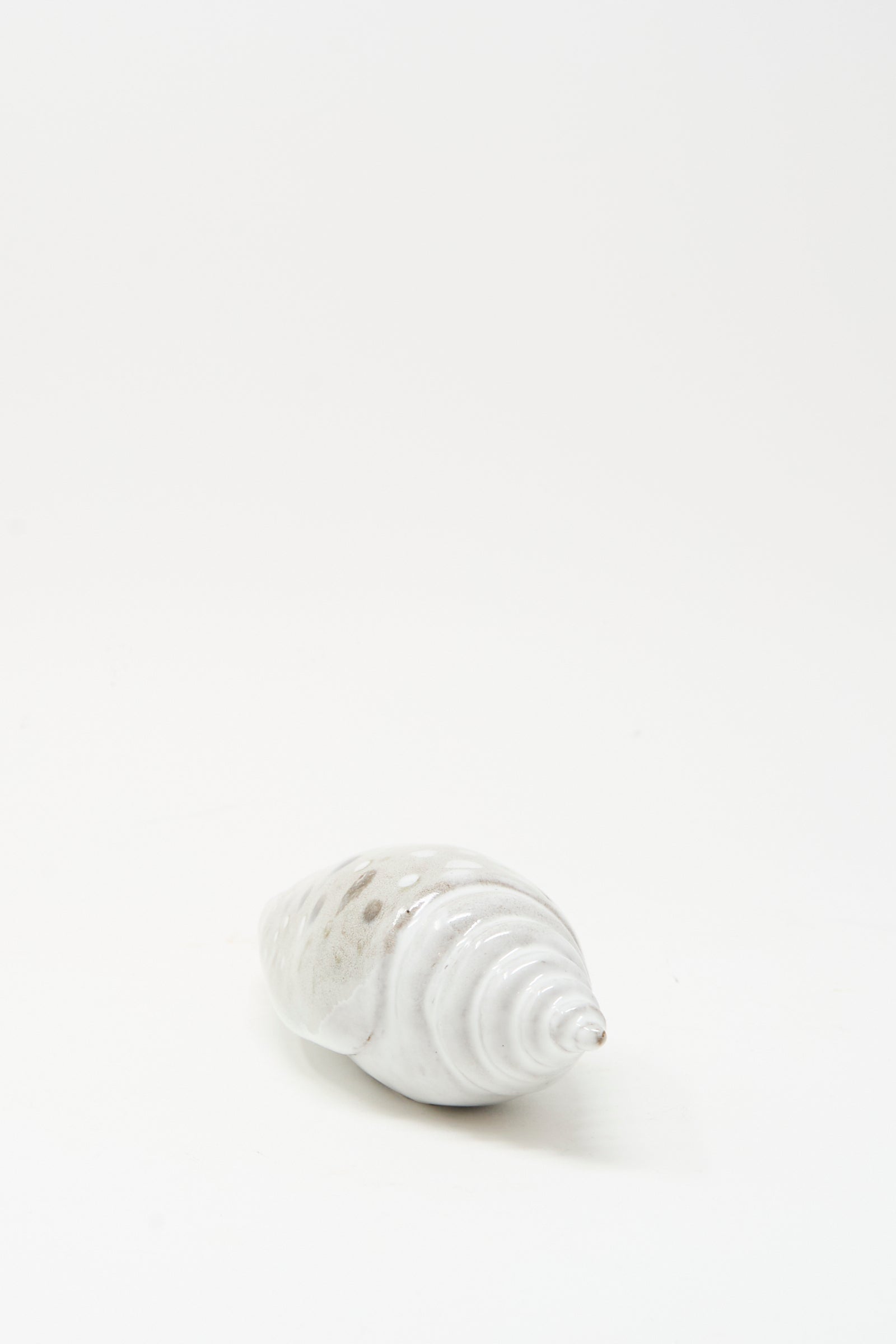 The E.C.C.E Shell Rattle XCV, a handmade white ceramic piece with subtle brown spots, is displayed on a plain white background.