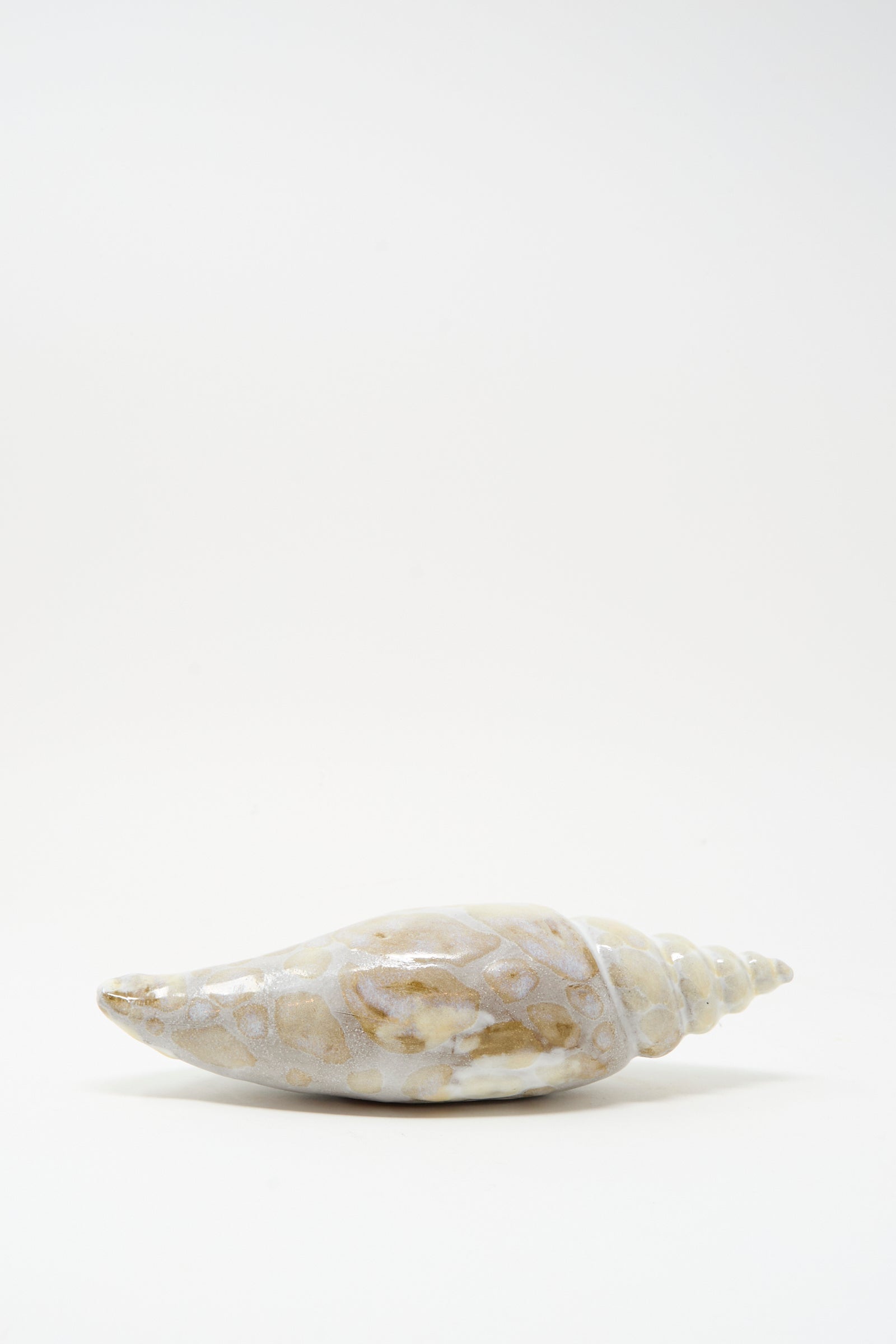 The Shell Rattle XCVII by E.C.C.E is a handmade beige and white ceramic shell, displayed horizontally on a plain white background.