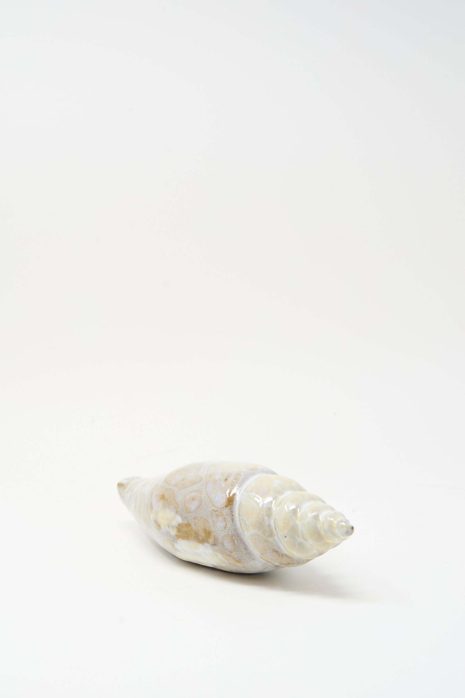 The E.C.C.E Shell Rattle XCVII, a handmade conical ceramic shell with a spiral tip and light brown spots, is displayed on a plain white background.