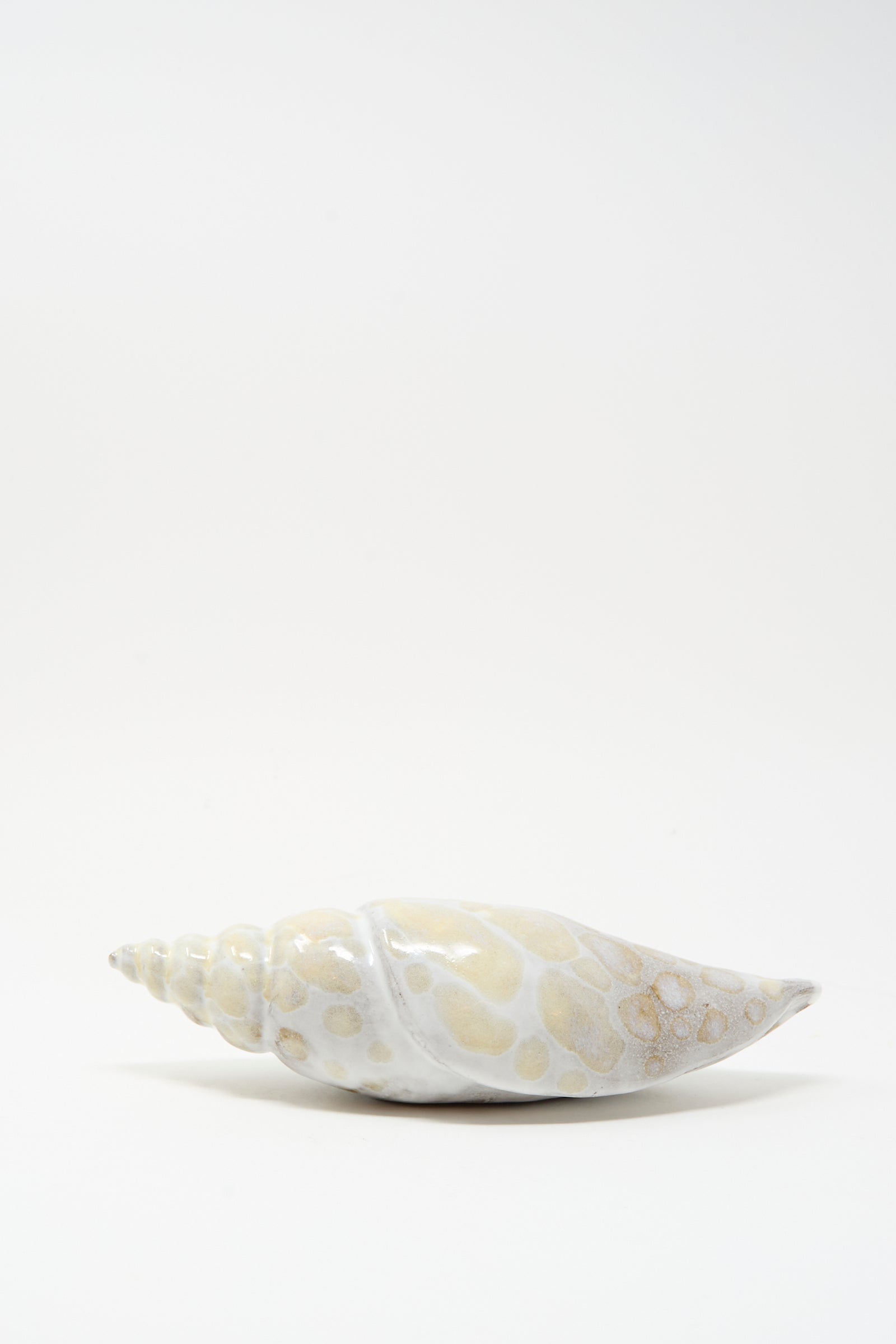The E.C.C.E Shell Rattle XCVII, a handmade light-toned ceramic piece with a spiral form, is displayed against a plain white background.