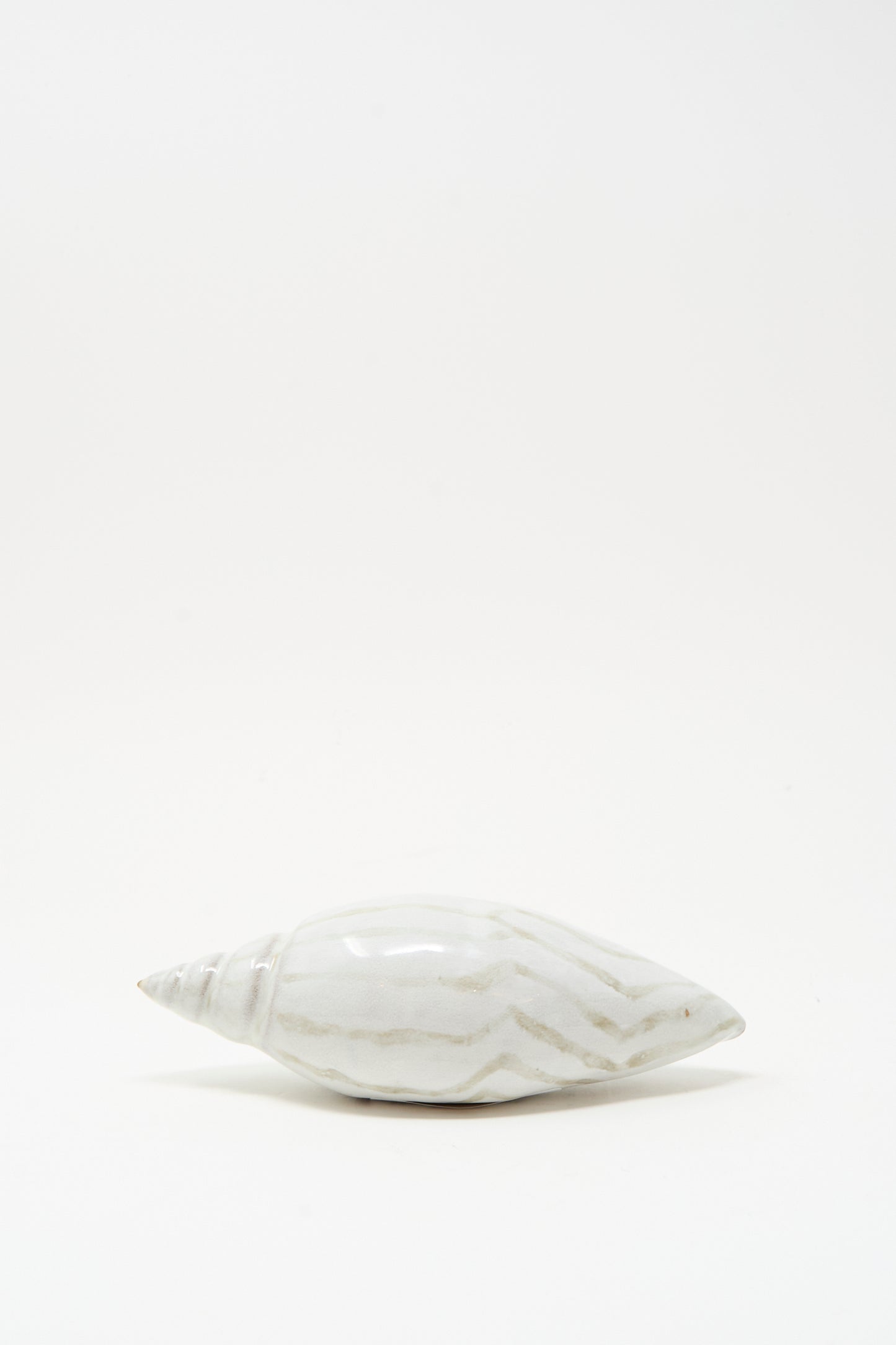 The Shell Rattle LXXVII by E.C.C.E features a handmade ceramic shell with light brown streaks, displayed on a plain white background.