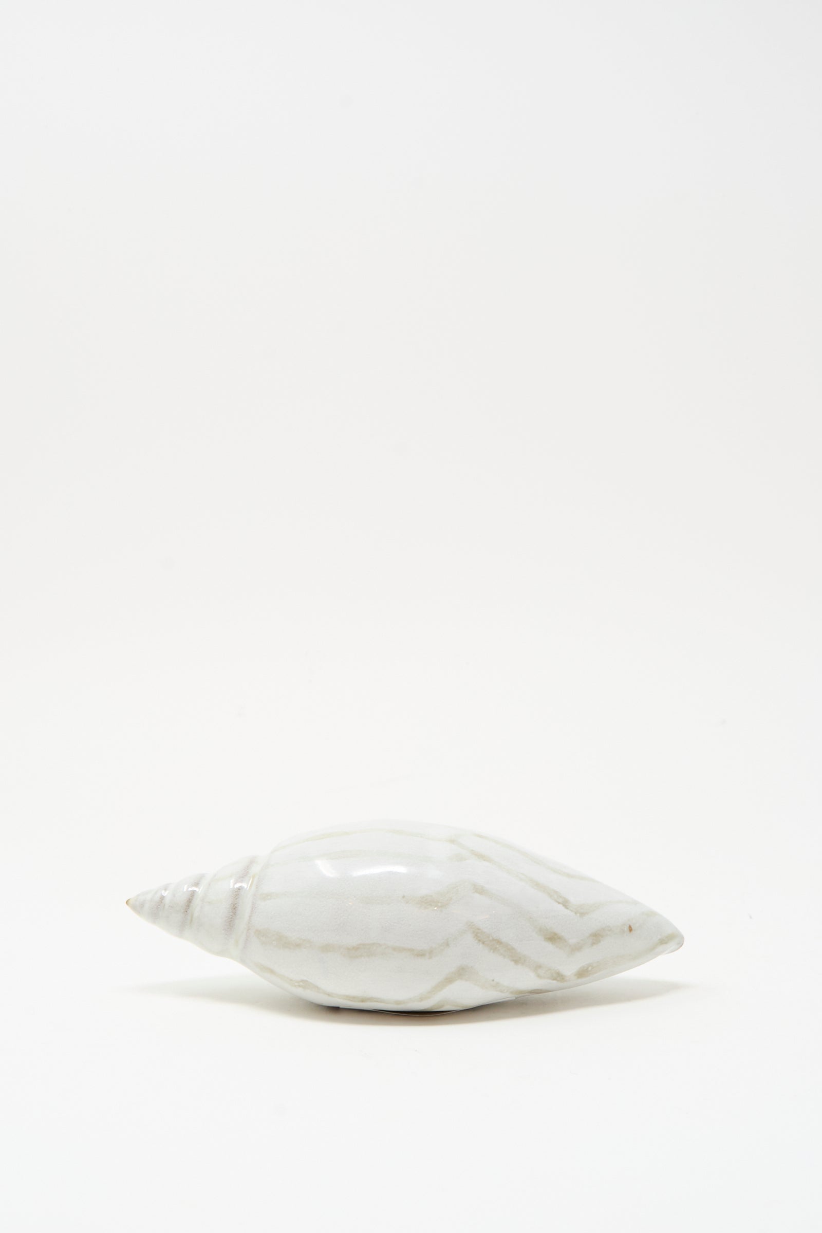 The Shell Rattle LXXVII by E.C.C.E features a handmade ceramic shell with light brown streaks, displayed on a plain white background.