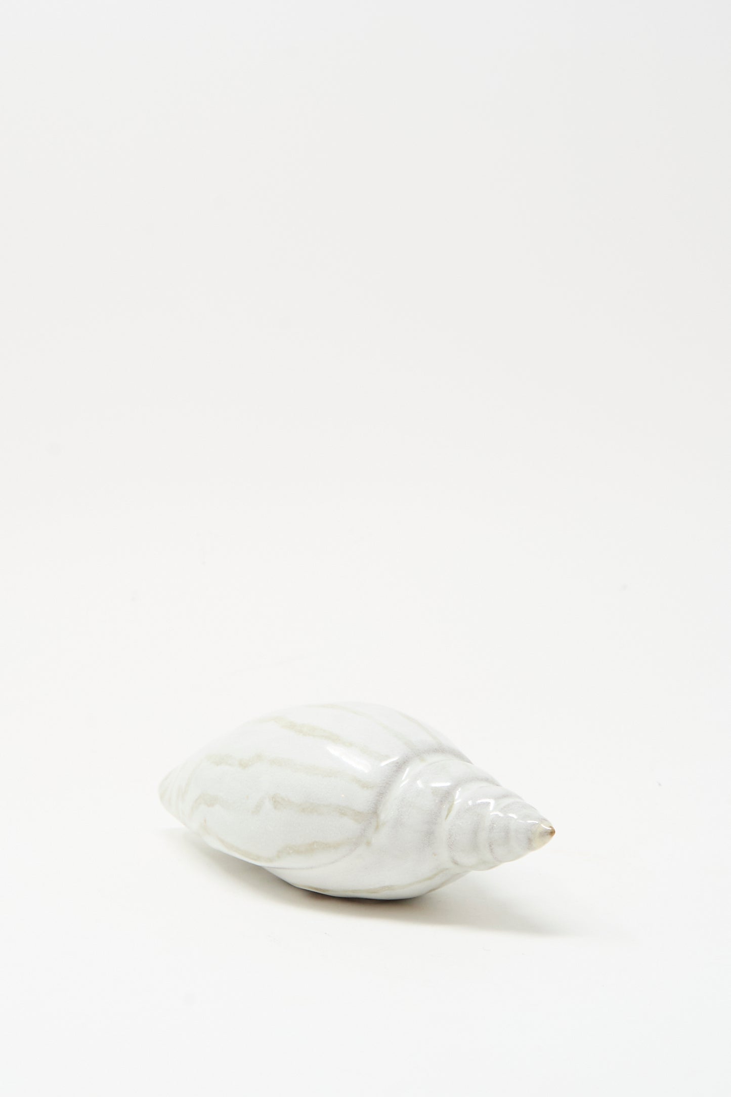 The E.C.C.E Shell Rattle LXXVII, a handmade white ceramic piece with subtle stripes, is displayed on a plain, light background.