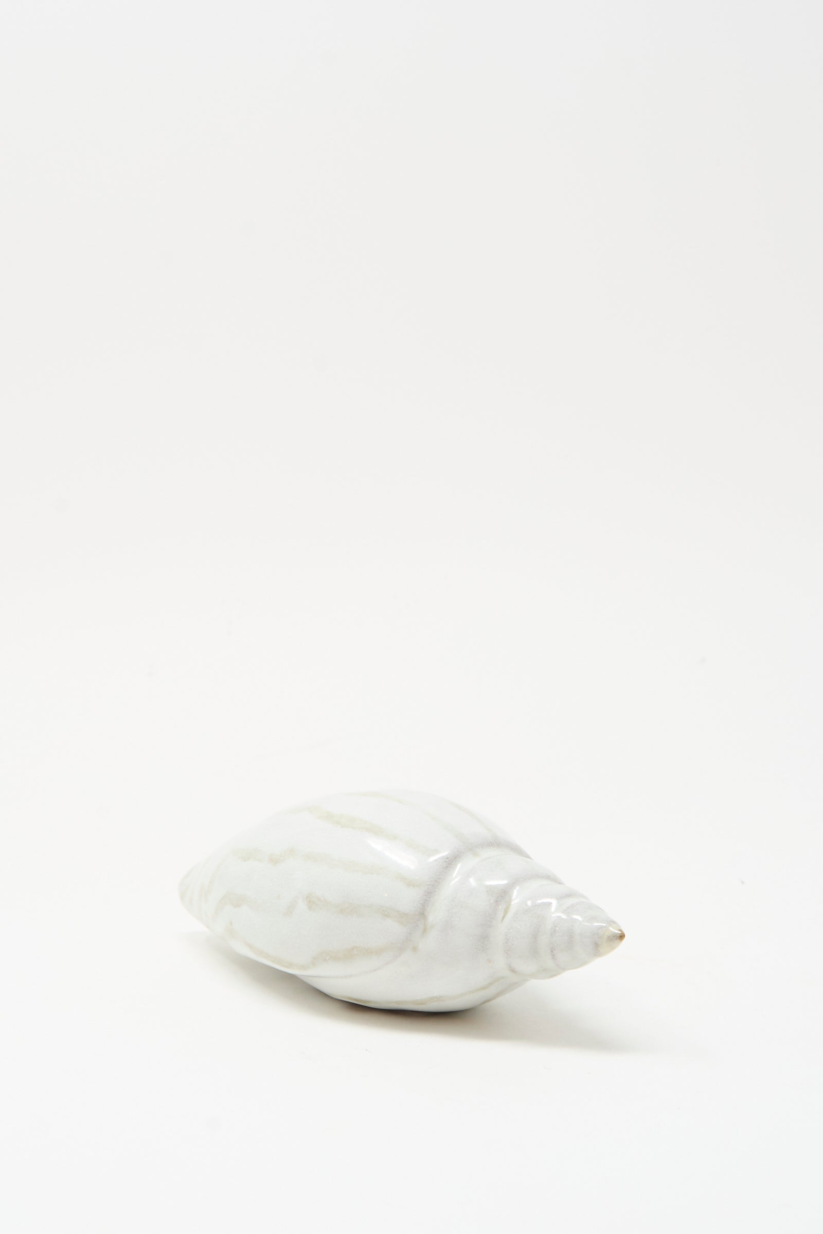 The E.C.C.E Shell Rattle LXXVII, a handmade white ceramic piece with subtle stripes, is displayed on a plain, light background.