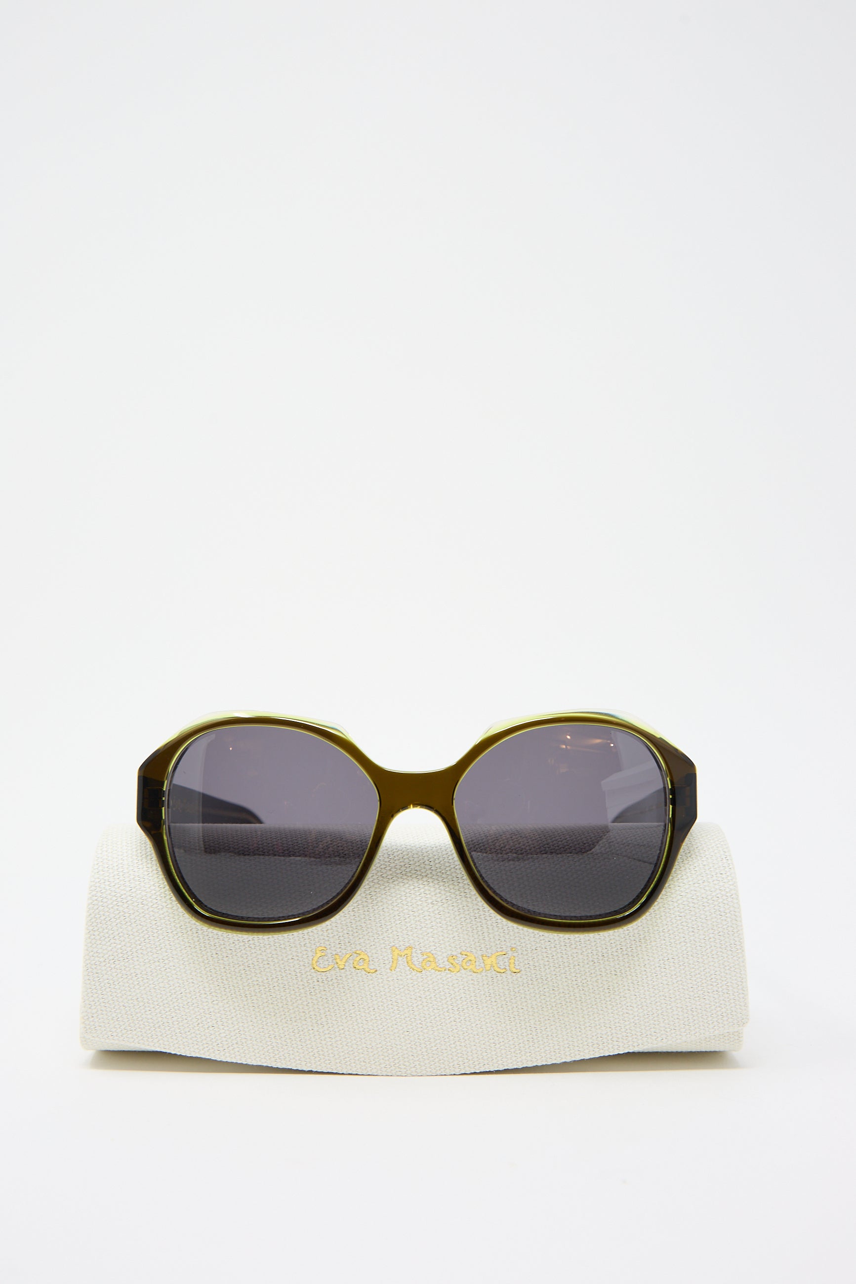 A pair of Eva Masaki 001 Sunglasses in Greens with a green cellulose acetate frame, displayed on a white fabric case with gold lettering, ensuring both style and UV protection.