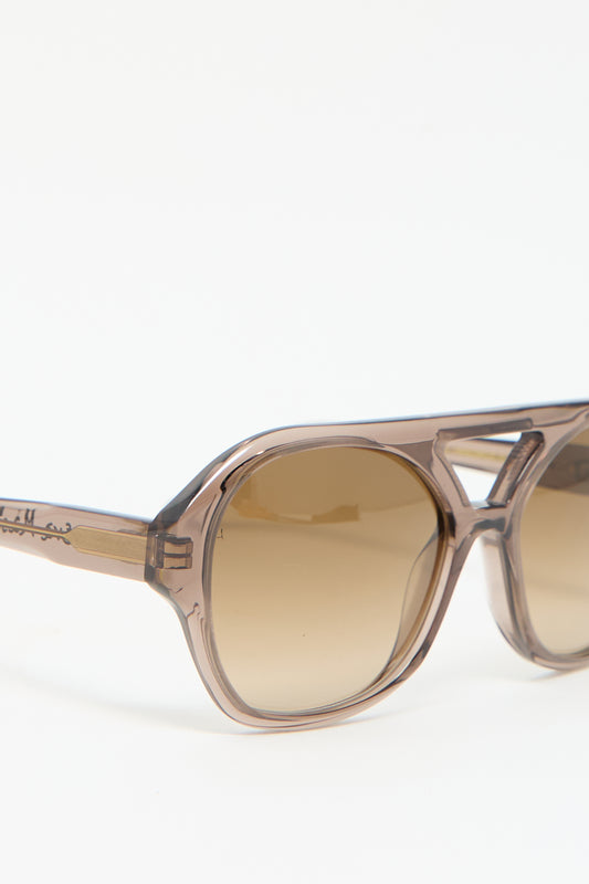 A close-up of Chiyo Aviator Sunglasses in Shroom by Eva Masaki, showcasing transparent brown square frames made from luxurious Italian acetate and featuring tinted lenses against a plain background.