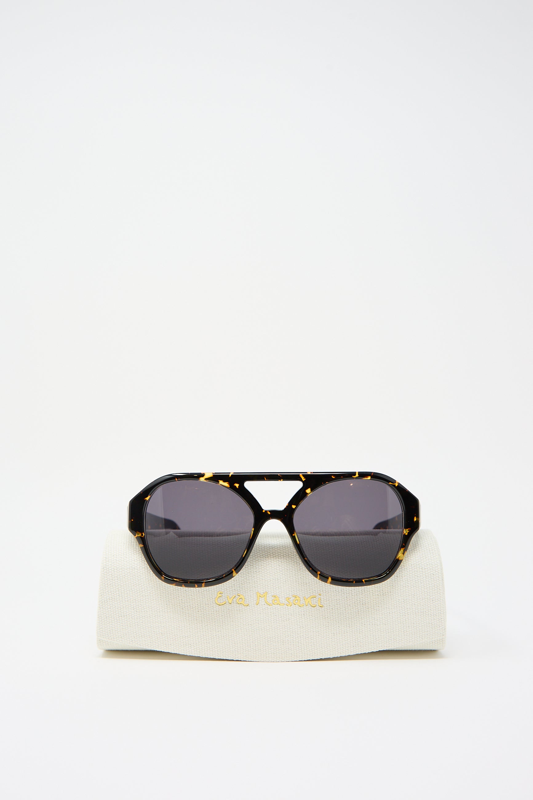 Chiyo Aviator Sunglasses in Gotham by Eva Masaki, made from luxurious Italian acetate, sit atop a white case with gold lettering.