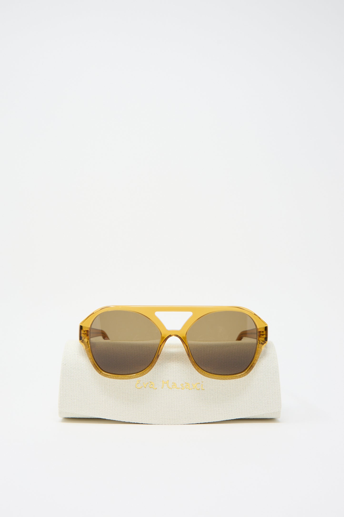 Chiyo Aviator Sunglasses in Honey by Eva Masaki are displayed on a white case with gold lettering against a plain white background, showcasing both their stylish design and UV protection.