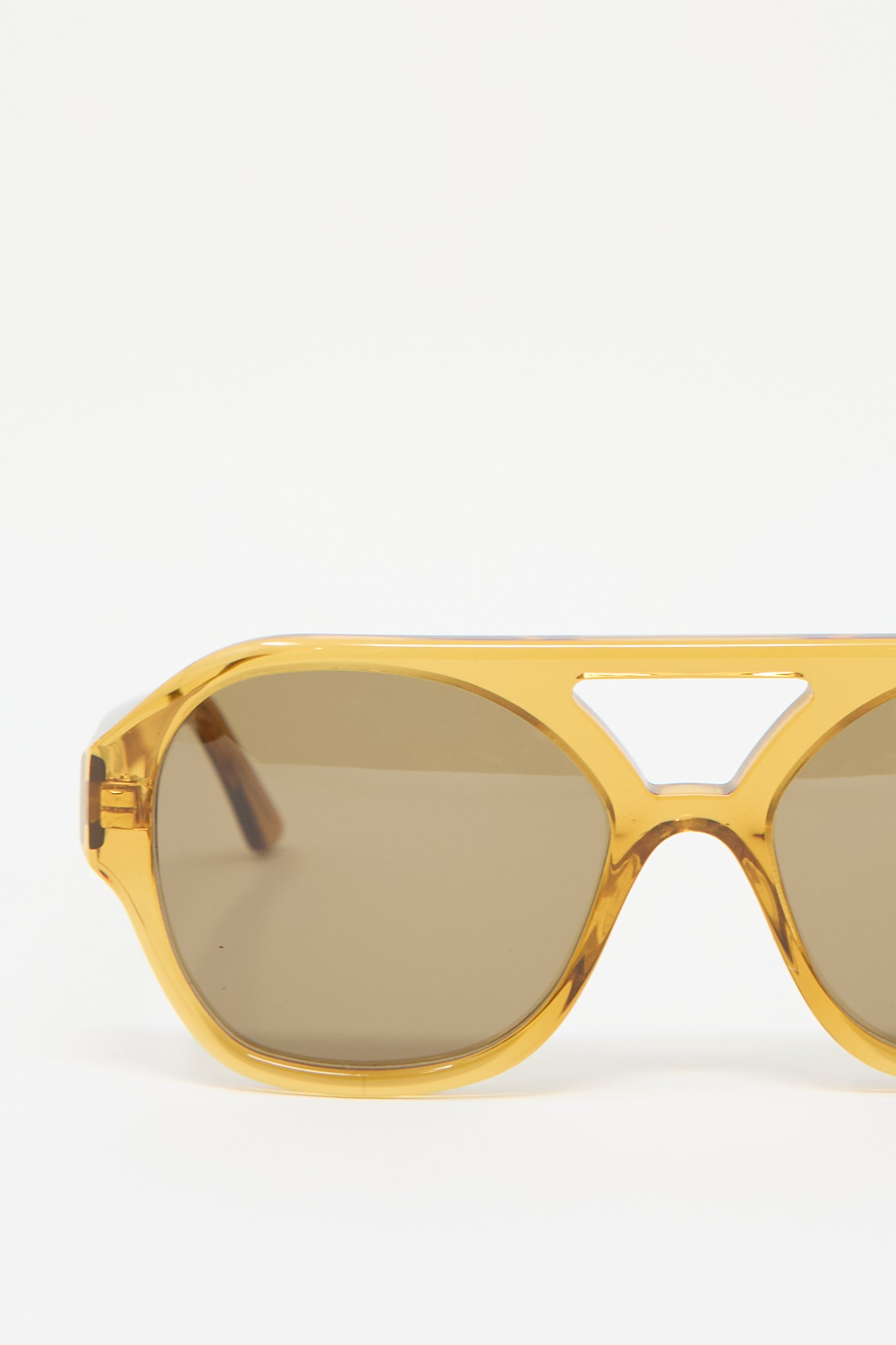 The Eva Masaki Chiyo Aviator Sunglasses in Honey feature an oversized hexagonal frame crafted from Italian acetate; showcasing a yellow, translucent finish and brown tinted lenses that offer 100% UV protection, all set against a plain white background.