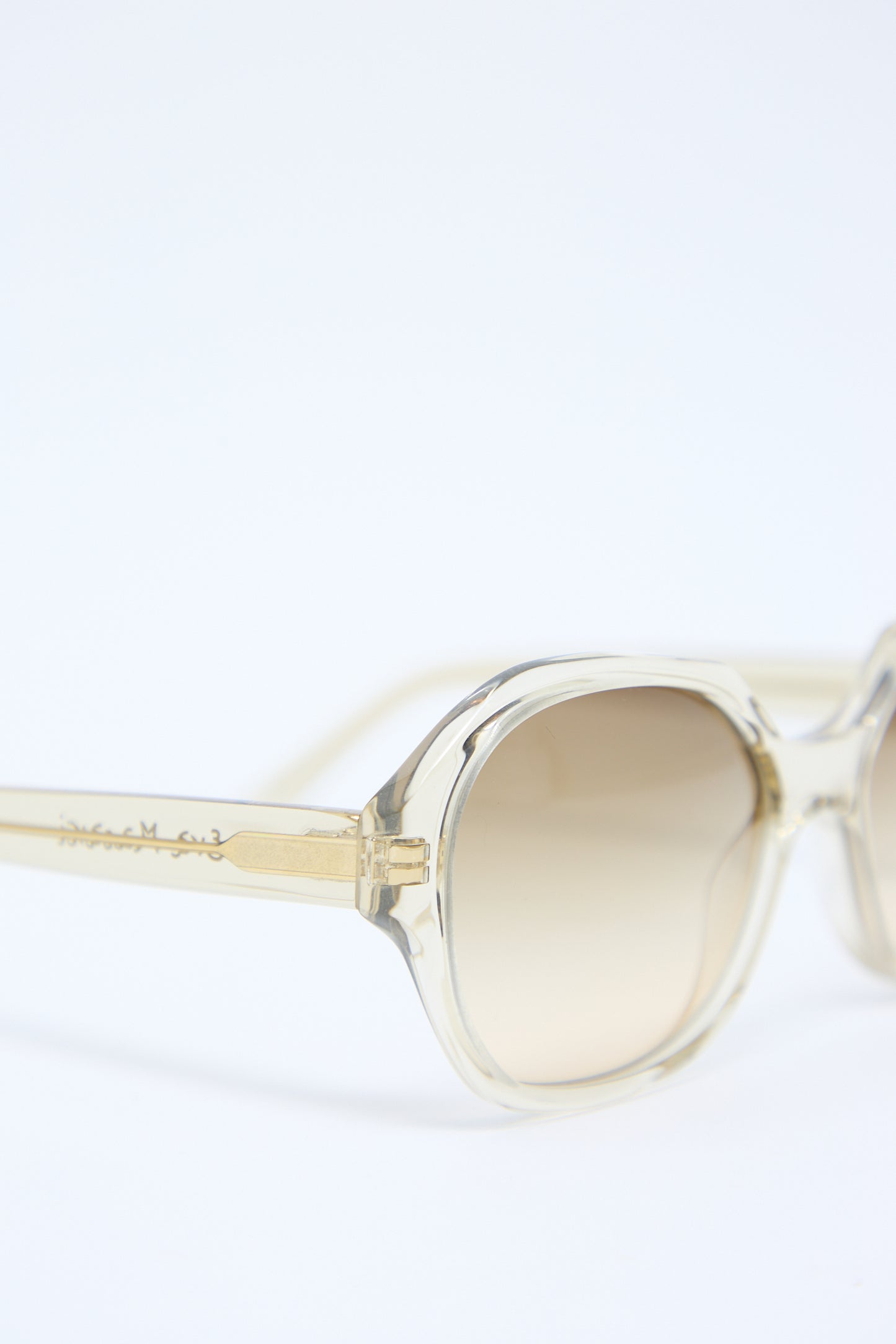 Close-up of Eva Masaki 001 Sunglasses in Toast with light brown tinted Zeiss lenses and a gold detail on the arm, featuring engraved text. The background is plain and white.