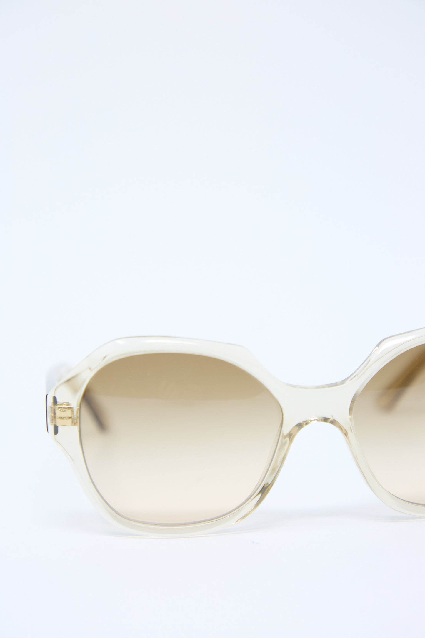 A pair of Eva Masaki 001 Sunglasses in Toast with an oversized hexagonal frame features clear arms and light brown tinted Zeiss lenses, set against a pristine white background.