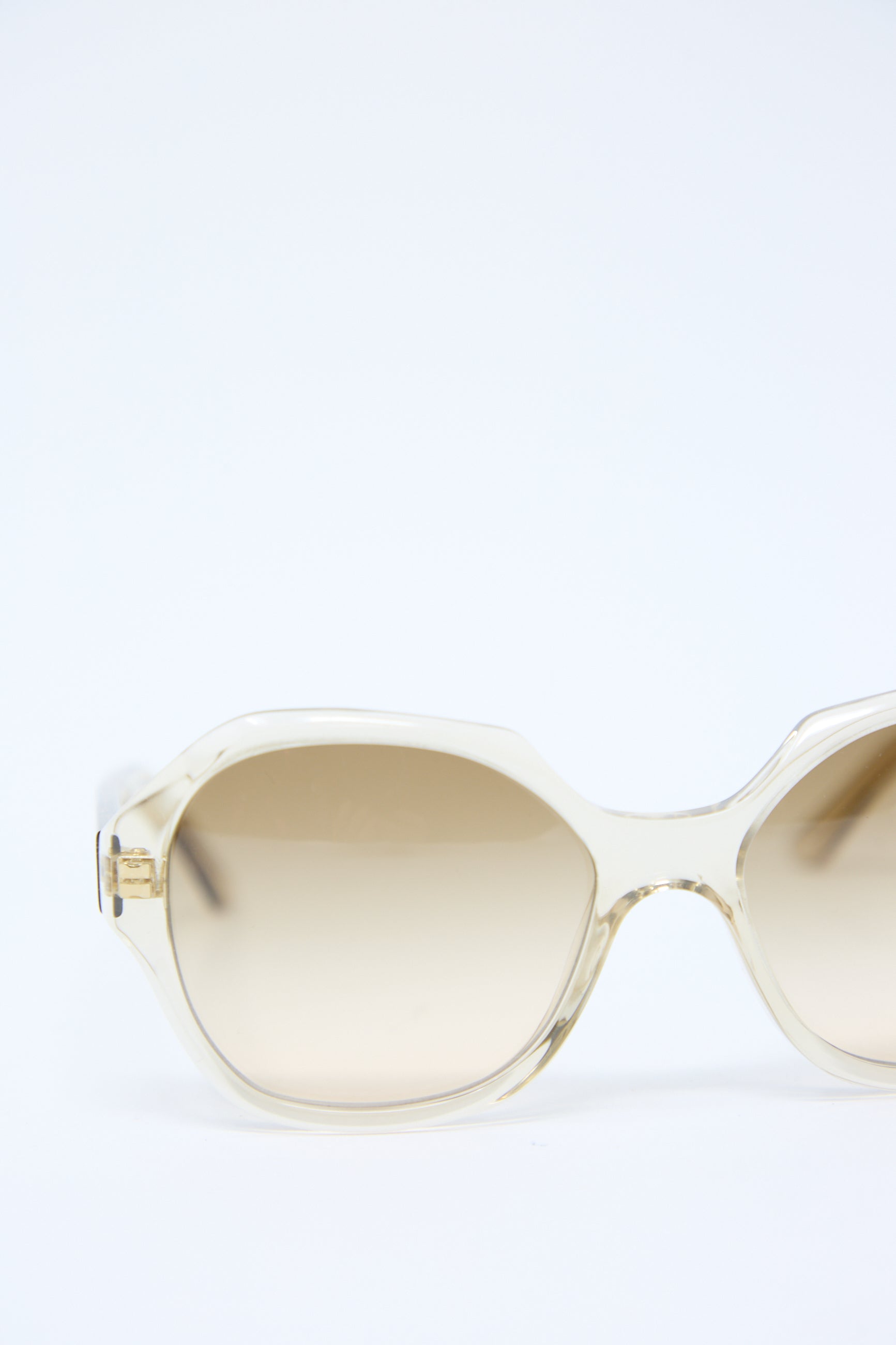 A pair of Eva Masaki 001 Sunglasses in Toast with an oversized hexagonal frame features clear arms and light brown tinted Zeiss lenses, set against a pristine white background.